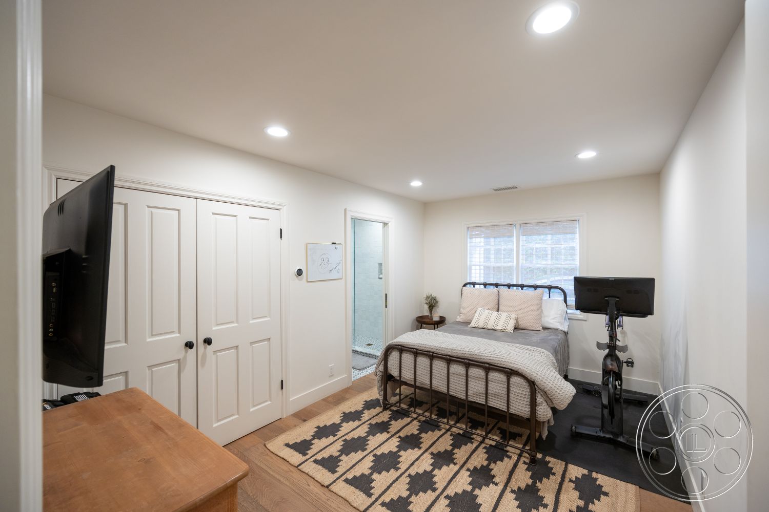 Americana 201 - modern light fixtures, natural light from windows, textured wall treatment, hardwood bedroom floors, white painted walls, rectangular area rug, spacious master bedroom, queen-size metal bed frame, built-in closet with double doors, exercise bike placement, simple yet functional room layout