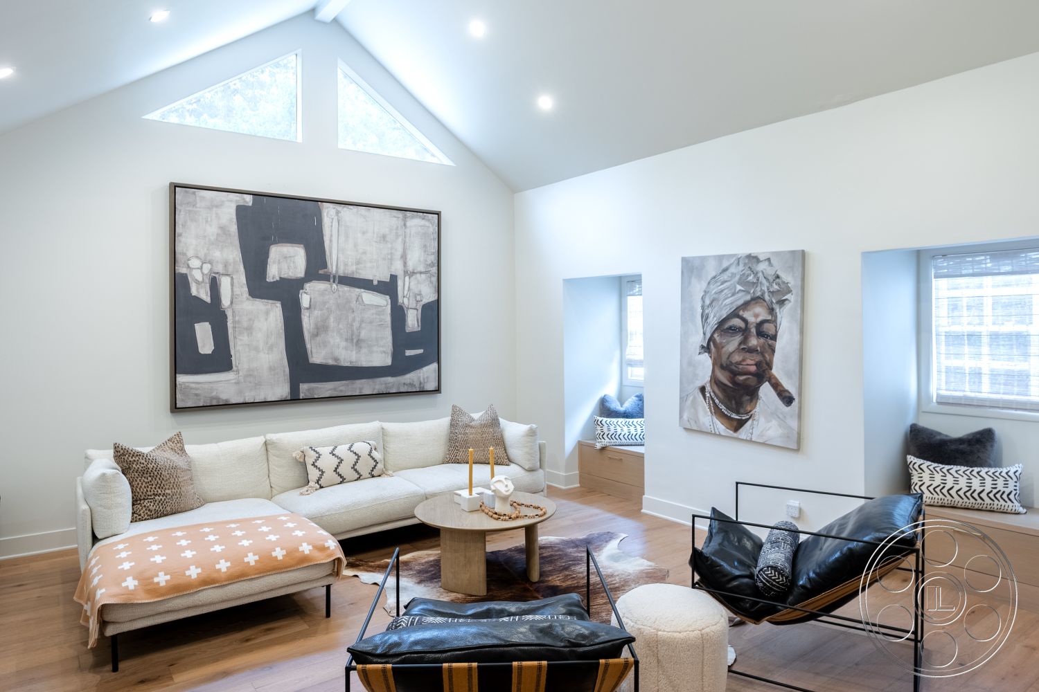 Americana 201 - neutral color palette, textured area rug, open floor plan, contemporary art on walls, minimalist coffee table, exposed wood ceiling beams, hardwood living room floors, interior living room, white painted walls, large windows with natural light, vaulted ceiling with triangular skylights, modern sectional sofa with throw blanket, black leather lounge chair with metal frame, benches with built-in storage