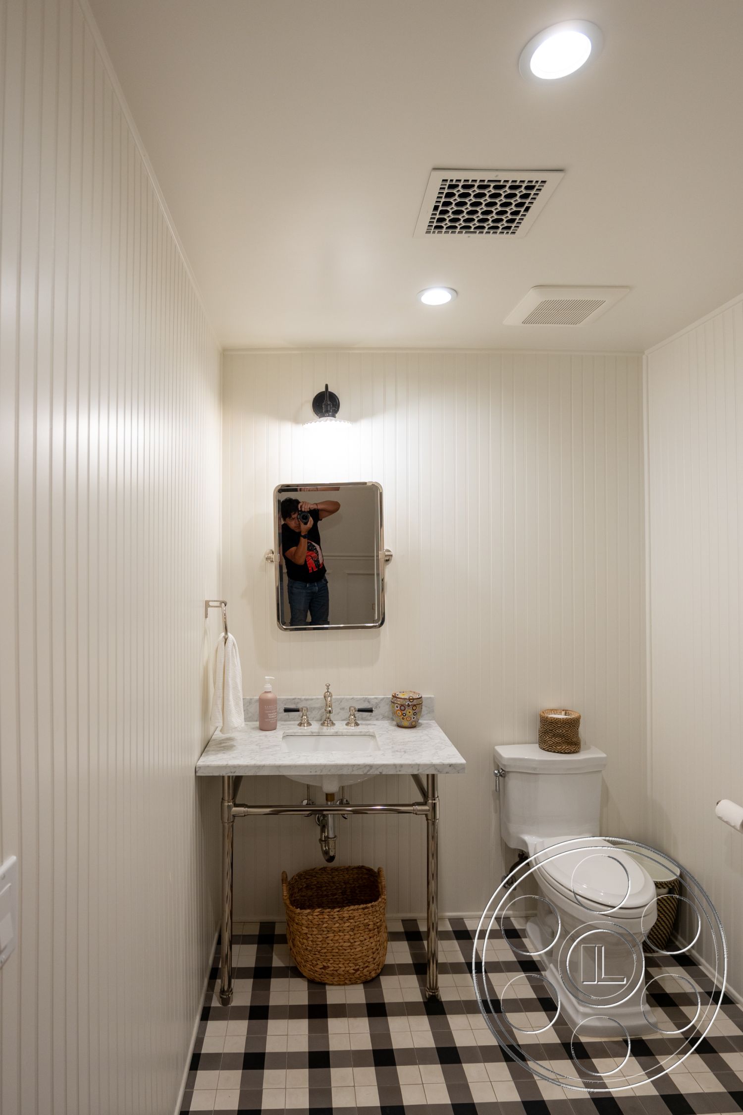 Americana 201 - woven storage basket, interior bathroom design, exposed plumbing fixtures, minimalist bathroom decor, marble bathroom countertop, white ceramic toilet, modern wall-mounted light fixture, white painted tongue and groove wall treatment, checkered tile bathroom flooring, rectangular mirror above vanity, stainless steel vanity support structure