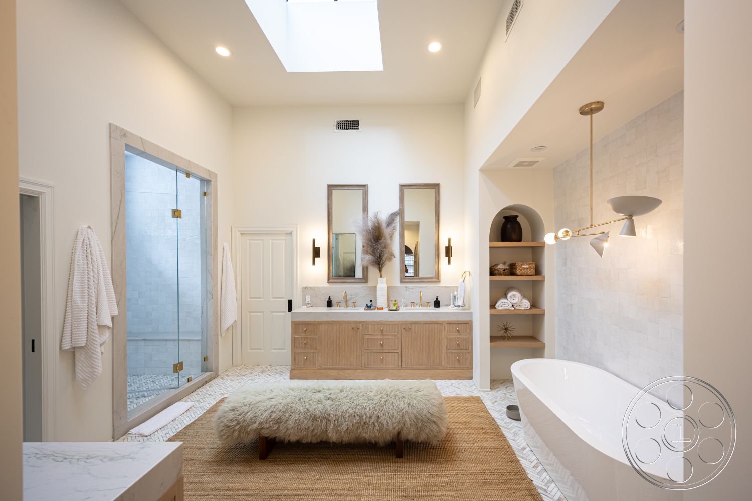 Americana 201 - minimalist decor, neutral color palette, gold pendant lighting, textured plaster walls, glass shower doors, natural fiber area rug, interior bathroom, white painted walls, freestanding soaking tub, skylight for natural light, concrete bathroom flooring, modern faucet fixtures, wood vanity cabinet, crown molding details, marble shower walls, double sink countertop, decorative shelving unit, large mirror above vanity, soft bath towels, arched niche for storage, towel hooks on door