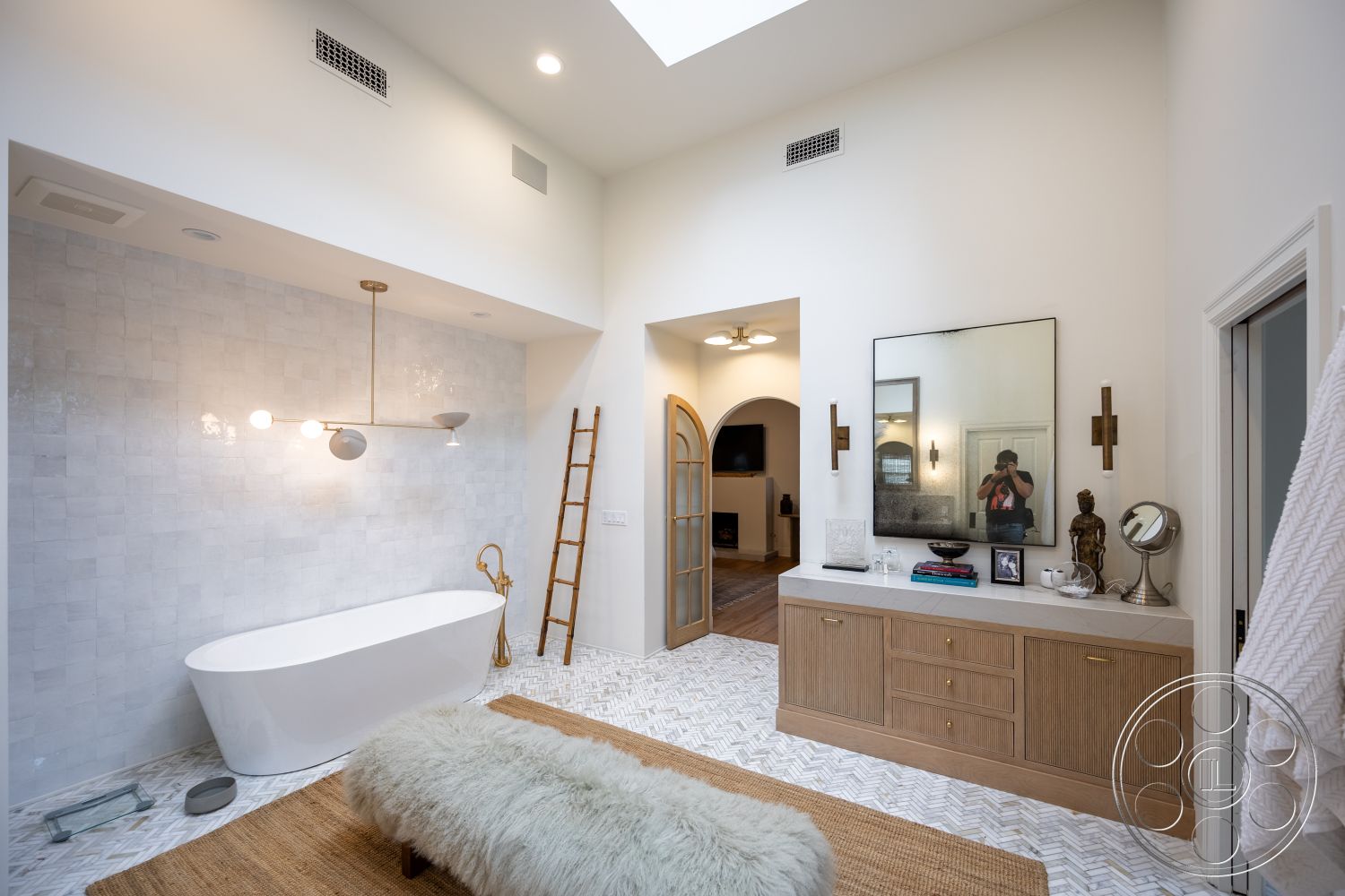 Americana 201 - interior recessed lighting, interior floor-to-ceiling window, interior natural fiber area rug, interior bright and airy atmosphere, interior minimalist bathroom design, interior marble tile bathroom walls, interior herringbone patterned marble bathroom flooring, interior freestanding soaking tub, interior contemporary light fixture, interior wooden ladder accent decor, interior oversized wall mirror, interior wooden cabinetry with gold hardware, interior plush faux fur bench, interior sculptural decorative elements, interior textured white walls, interior open archway leading to living area