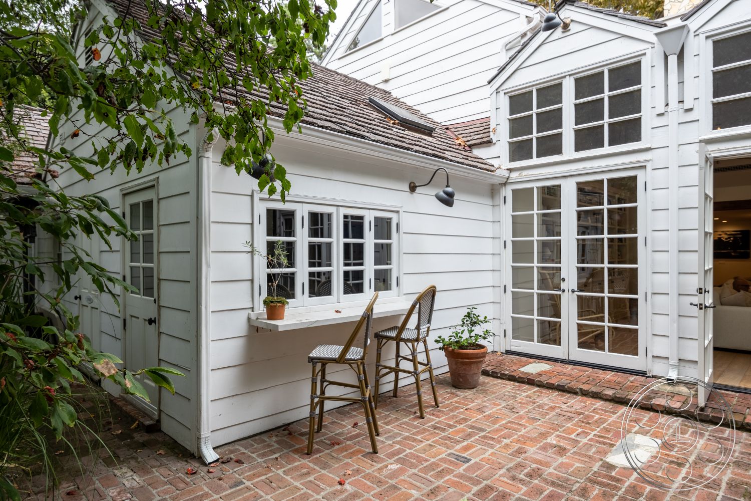 Americana 201 - large windows, exterior, lush greenery, potted plants, outdoor seating area, double French doors, traditional architectural style, garden atmosphere, gable roof, brick patio flooring, exposed light fixture, courtyard setting, wood siding walls, adjoining indoor space