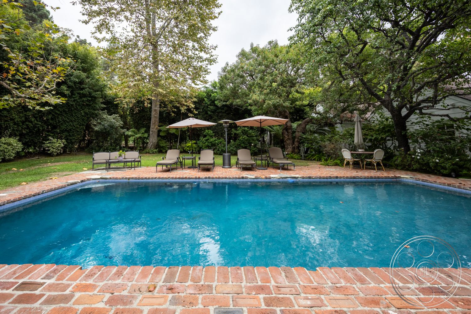 Americana 201 - rectangular swimming pool, interior-exterior flow, outdoor lounge area, natural stone pathway, lush greenery backdrop, landscaped garden setting, concrete patio floor, brick pool border, poolside relaxation area, open-air relaxation space, metal lounge chairs, parasol shade umbrellas, brick paver pool deck, tropical garden ambiance