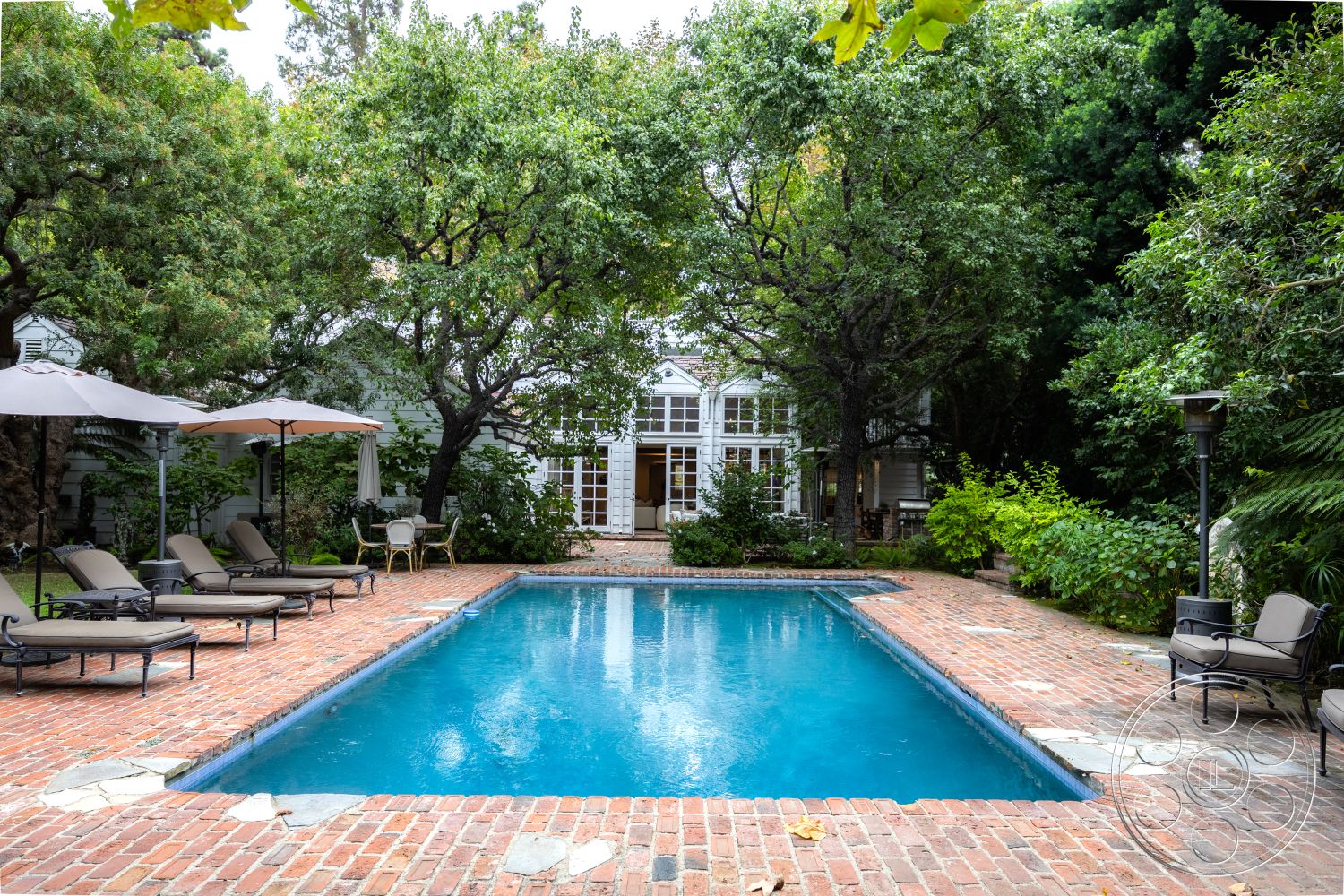 Americana 201 - rectangular swimming pool, cobblestone pathway, concrete pool border, surrounding tree canopy, lush garden landscape, wooden patio lounge chairs, brick pool patio, stone pool deck accents, exterior French doors, shaded outdoor umbrellas, outdoor lantern fixtures, interior view of residential home, pool area with natural scenery, exposed brick outdoor flooring