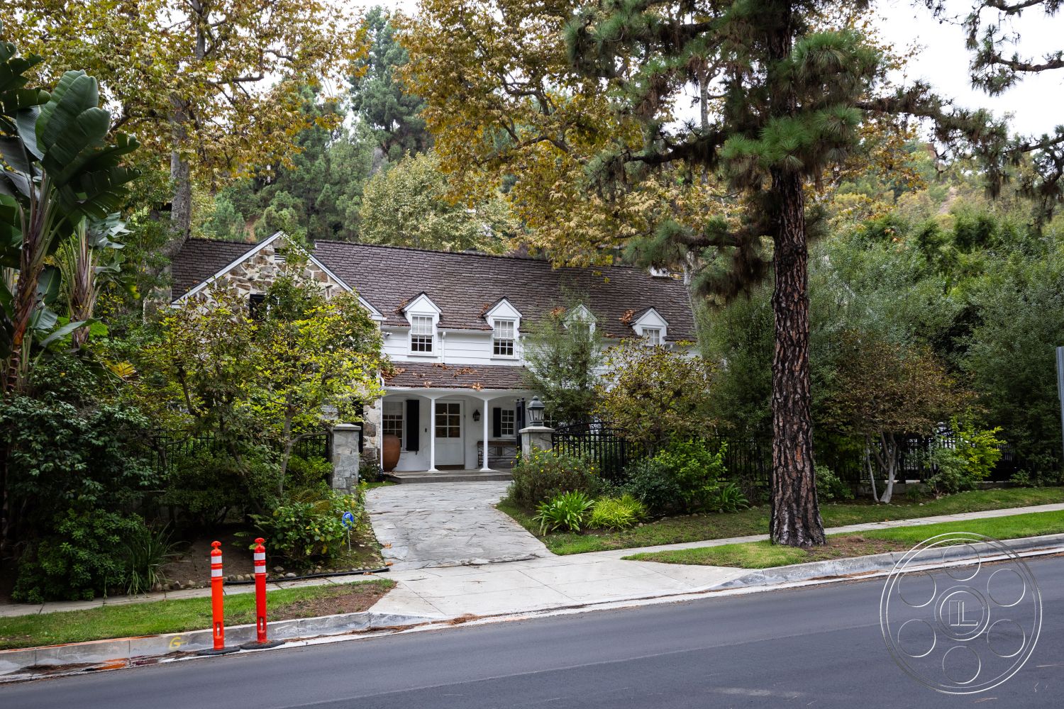 Americana 201 - lush greenery, tree-lined street, stone steps, wooden front door, double-hung windows, asphalt street, shingle roof, landscaped garden beds, front porch area, exterior stone facade, natural stone driveway, slate walkway, traditional gable roof, decorative fence panel, oak tree shading, modern porch lighting, rural suburban setting, traditional farmhouse style, circular driveway entry