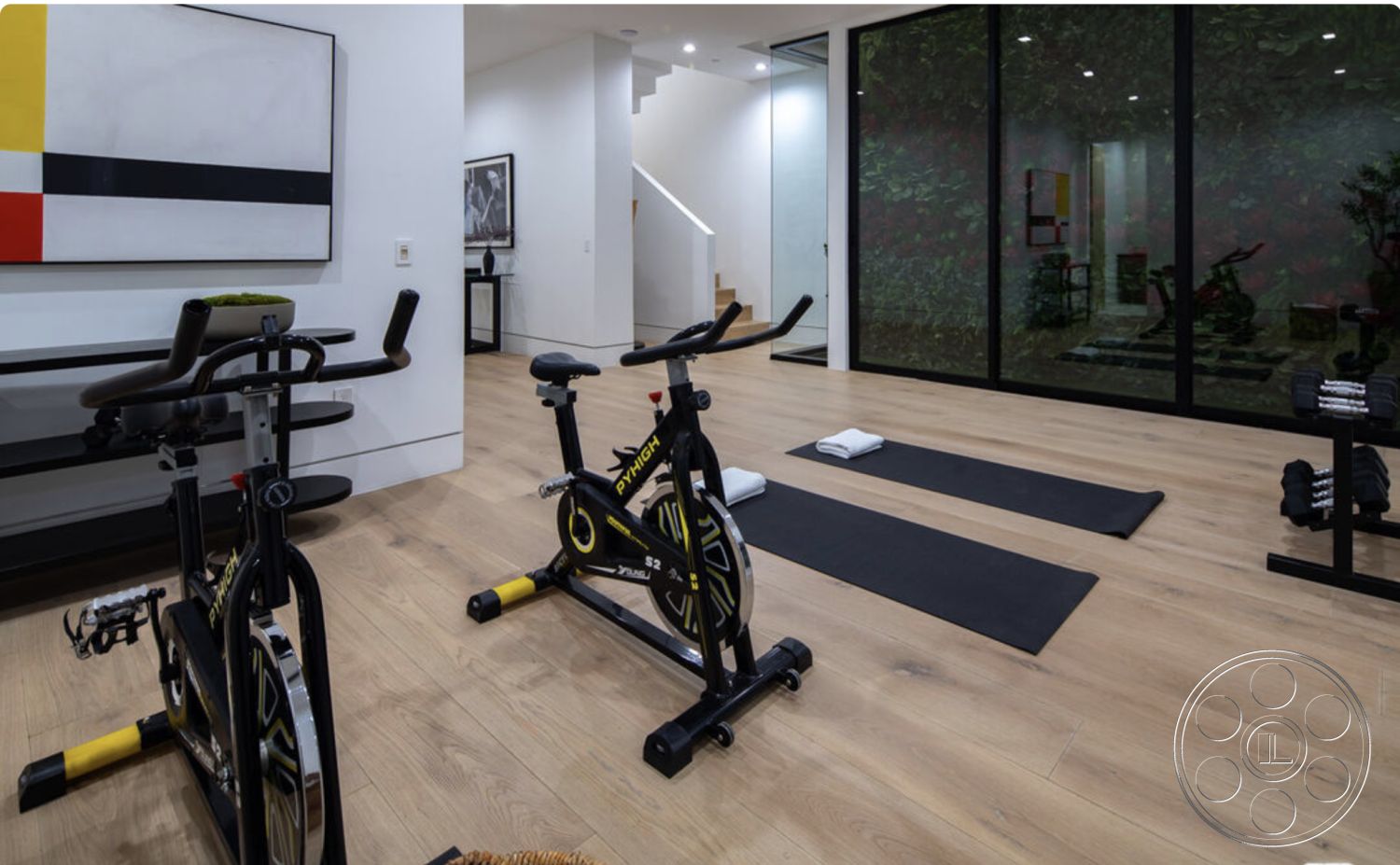 Modern 514 - light hardwood flooring, modern lighting fixtures, minimalist design elements, exercise bikes, black exercise equipment, neutral painted walls, glass wall partition, interior fitness room, multicolored abstract wall art, open stairwell with modern railings, yoga mats