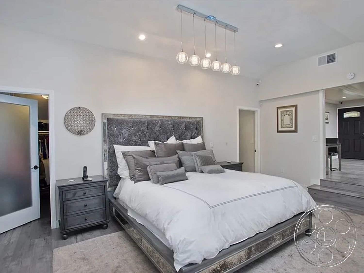 Americana 430 - neutral color palette, minimalist design, open layout, modern pendant lighting, master bedroom, frosted glass door, double door entry, contemporary interior, hardwood bedroom floors, white painted walls, framed artwork on wall, plush bedding with decorative pillows, textured fabric bed headboard, gray nightstand, vaulted bedroom ceiling