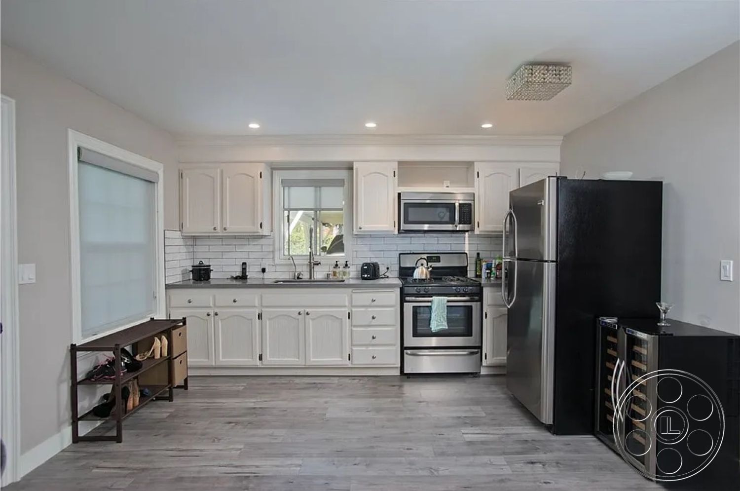 Americana 430 - stainless steel appliances, open shelving, under-cabinet lighting, neutral wall paint, interior kitchen, modern chandelier light fixture, white shaker kitchen cabinets, marble tile backsplash, vinyl plank kitchen flooring, single-basin kitchen sink, glass window with white trim, black refrigerator, wine cooler built-in, shoe storage bench