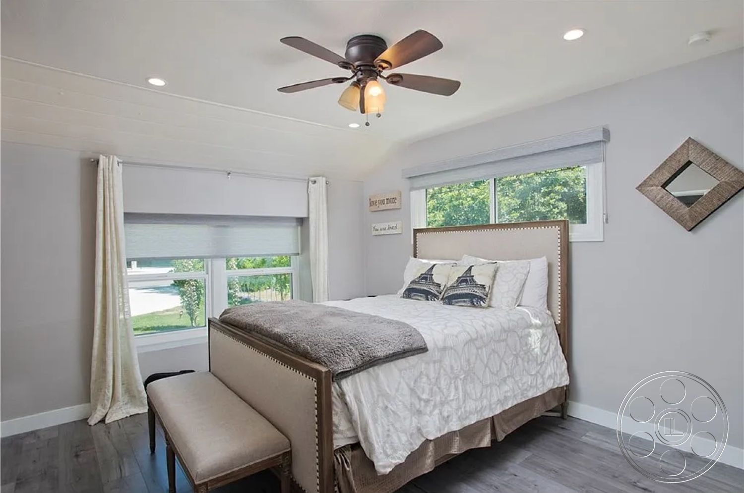 Americana 430 - hardwood bedroom floors, interior bedroom setting, painted grey walls, white ceiling with recessed lighting, modern bed frame with nailhead trim, textured throw blanket on bed, large windows with roller shades, window treatment curtains, decorative mirror on wall, ceiling fan with light fixture