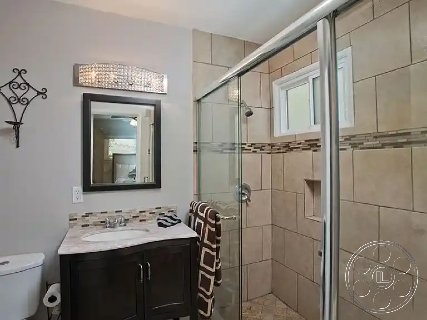 Americana 430 - contemporary styling, decorative wall sconce, modern mirror, glass shower doors, chrome shower fixtures, interior bathroom, built-in shower niche, white painted walls, tile bathroom walls, dark wood vanity cabinet, neutral tile flooring, marble bathroom countertop, mosaic tile accent strip