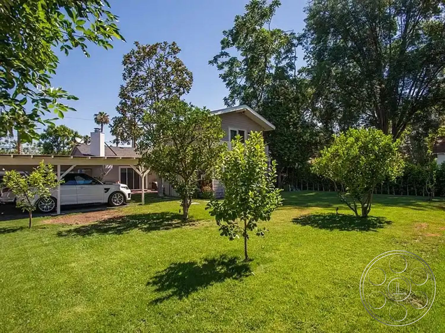 Americana 430 - single-story home, concrete driveway, urban residential area, sunlit garden, green grass lawn, residential setting, suburban backyard, open green space, leafy trees, exterior wooden siding, carport structure, shade garden, outdoor landscape, home with porch