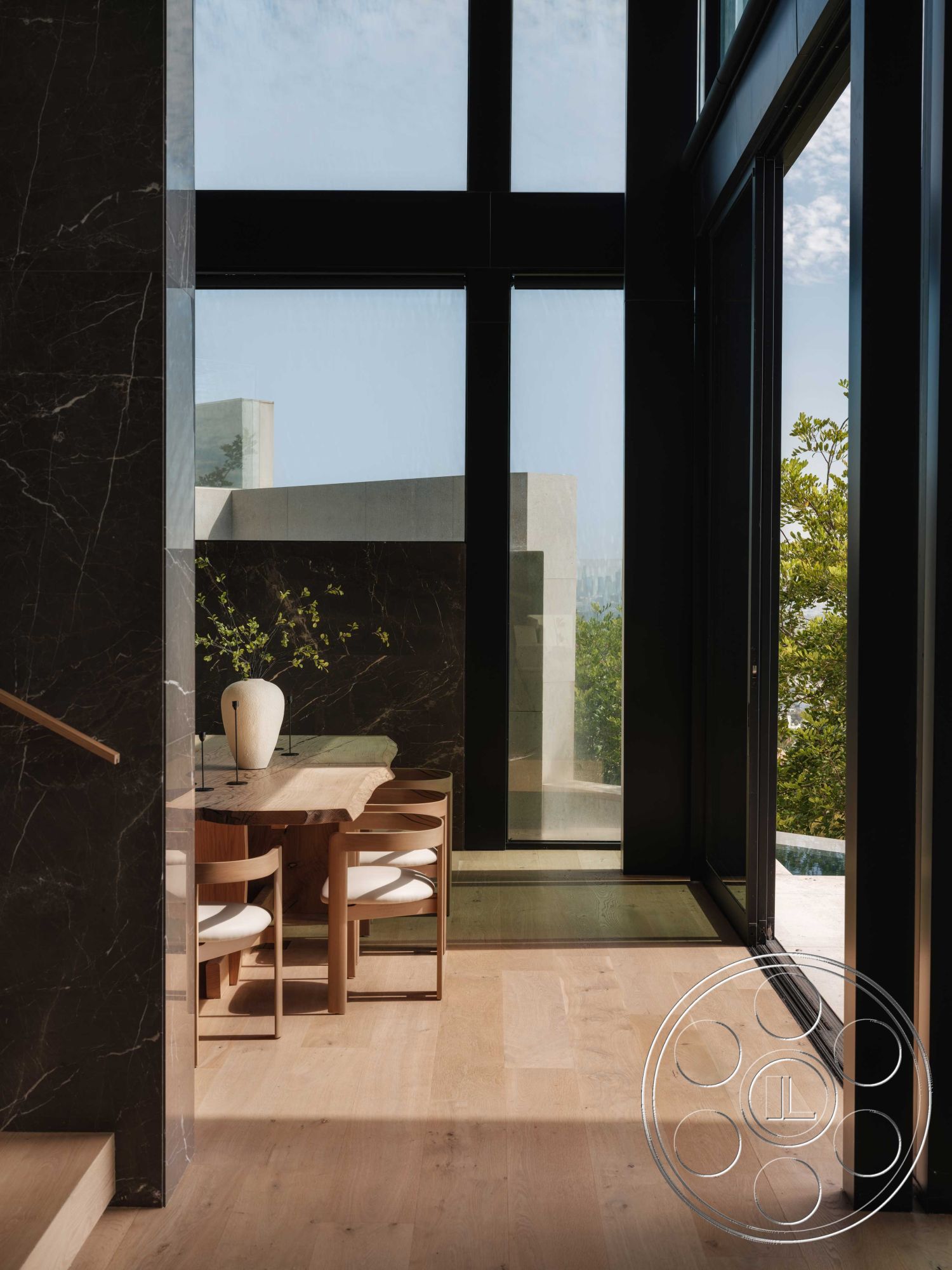 Modern 515 - natural wood dining table, seamless indoor-outdoor connection, contemporary architectural style, open-concept living area, modern minimalist design, natural light-filled space, minimalist dining area, glass floor-to-ceiling windows, lush outdoor greenery view, interior black marble wall, interior oak hardwood flooring, simple wooden dining chairs, elegant ceramic vase on table, casual elegant decor, natural materials blending, calming neutral color palette