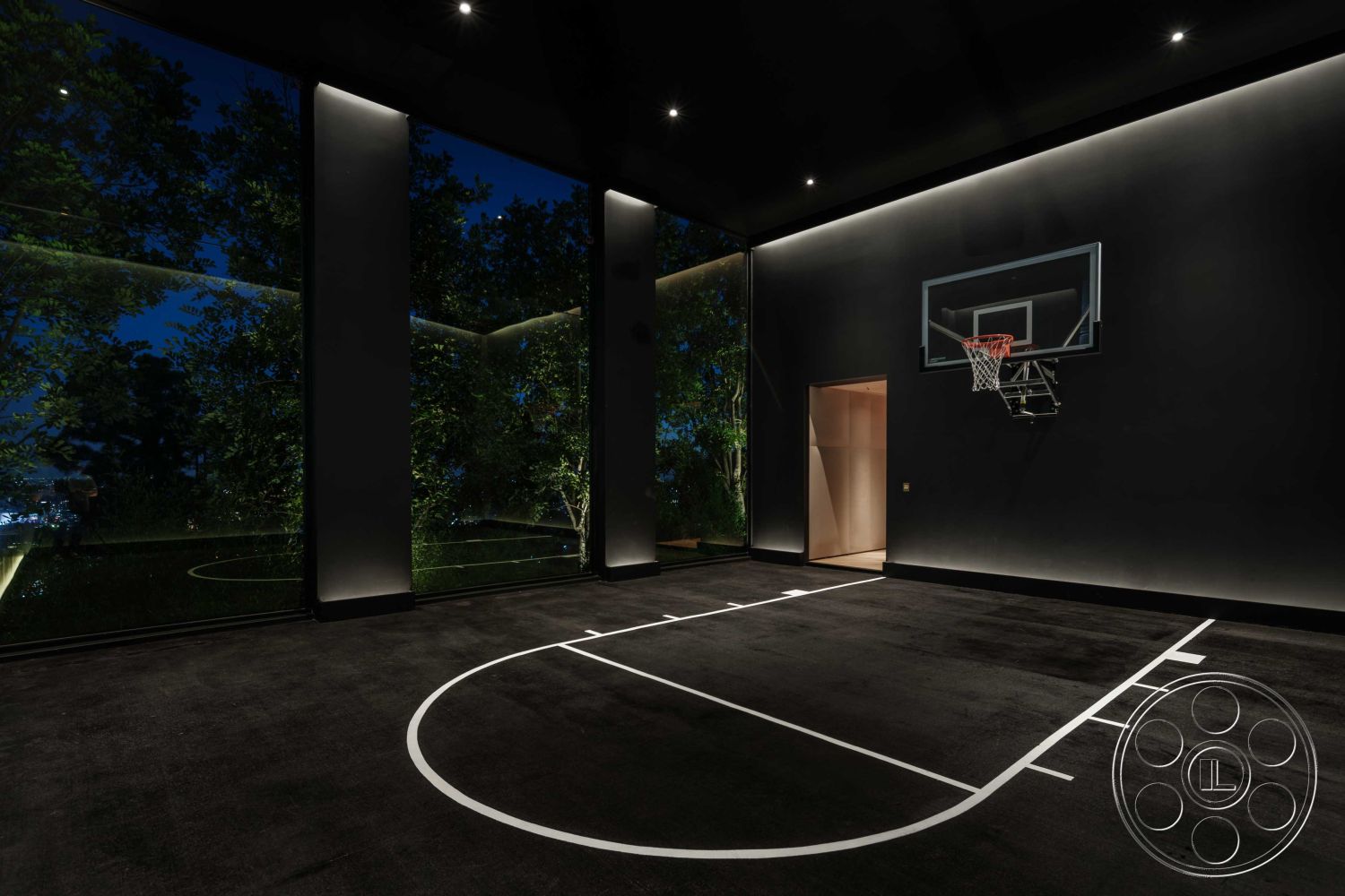Modern 515 - open floor plan, high ceiling, nighttime ambiance, contemporary design elements, dark walls, seamless indoor-outdoor connection, black rubber flooring, floor-to-ceiling glass windows, minimalist lighting fixtures, lush outdoor greenery view, interior basketball court, indoor sports area, modern basketball hoop, cozy space for recreation