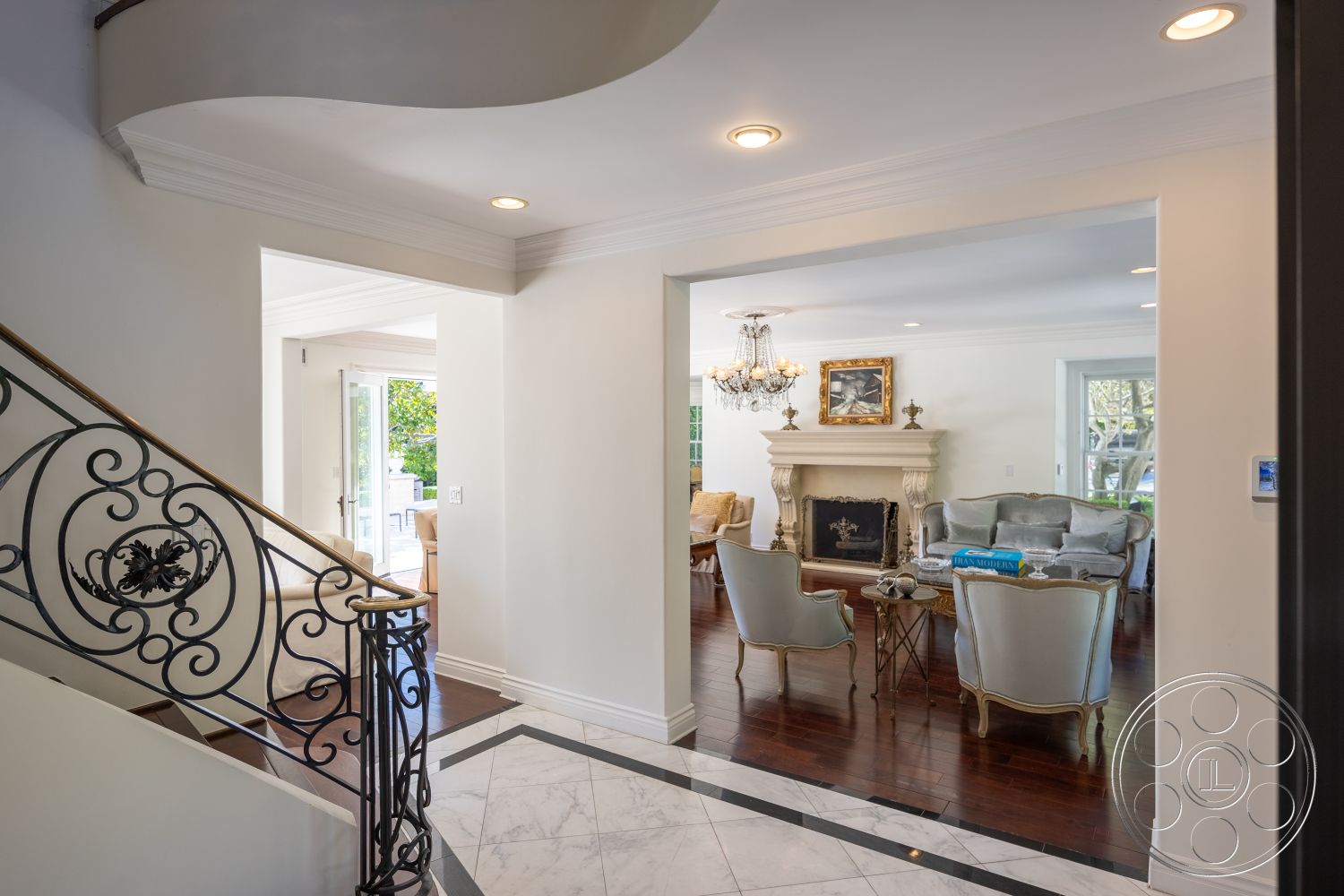 Americana 431 - interior hardwood living room floors, interior white painted walls, interior open floor plan, interior cozy seating area, interior decorative wall art, interior curved staircase, interior marble foyer floor, interior decorative iron staircase railings, interior ornate chandelier lighting, interior crown molding details, interior marble tile detail in entryway, interior coffered ceiling in living room, interior traditional fireplace surround