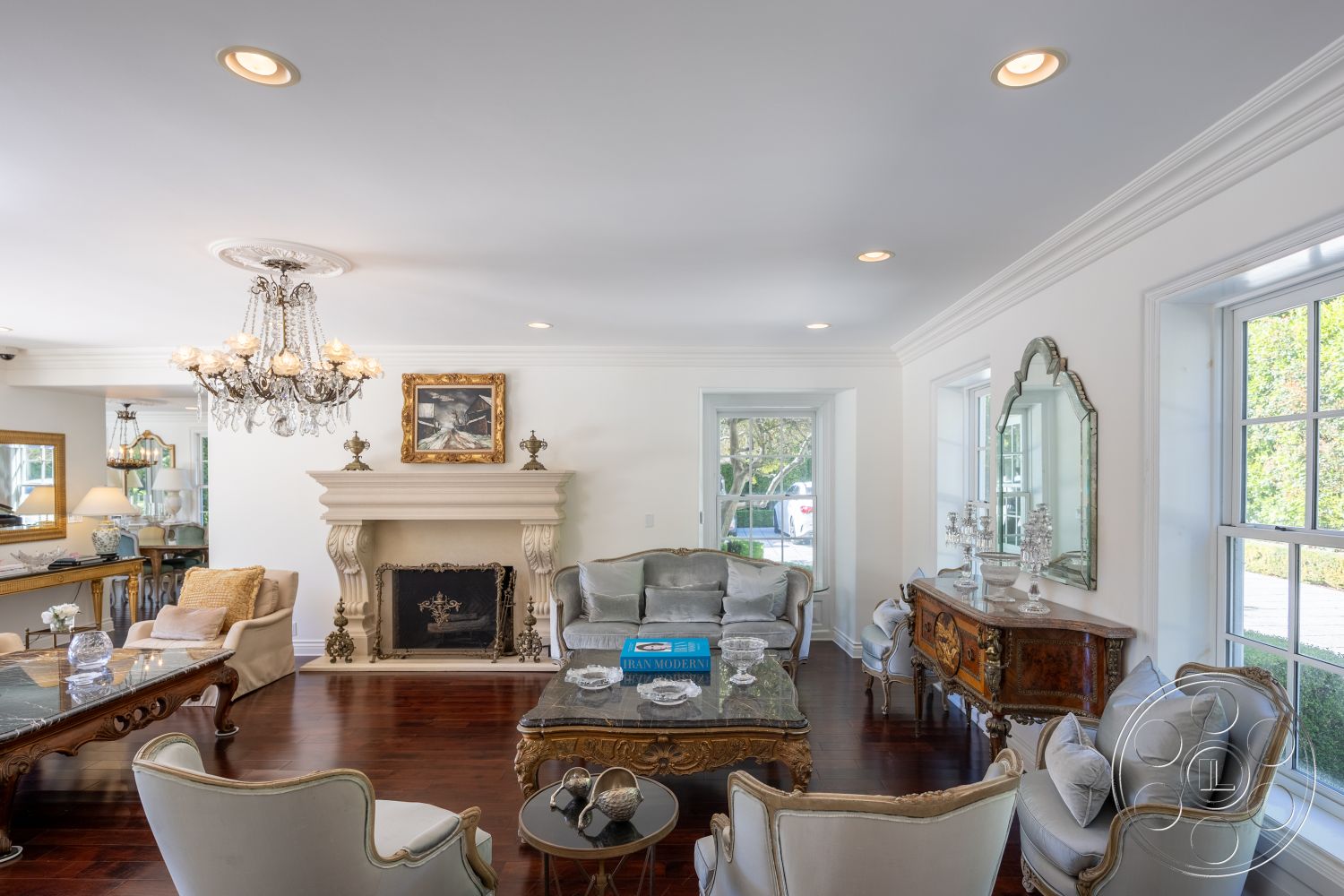 Americana 431 - neutral color palette, hardwood flooring, cozy seating arrangement, textured plaster walls, stylish armchairs, glass accent table, interior living room, marble fireplace surround, crown molding details, decorative mirror with ornate frame, exposed wood ceiling, chandelier lighting fixture, framed artwork on walls, large windows with white trim, traditional sofa with decorative pillows, antique wooden coffee table, elegant sideboard with glass decor, flush mount recessed lighting, gas fireplace with stone mantel