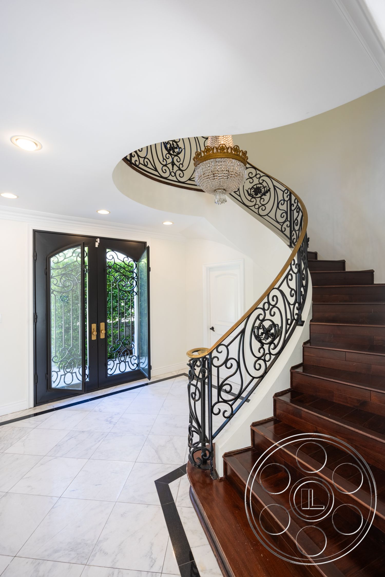 Americana 431 - elegant foyer, chandelier lighting fixture, interior entry foyer, spiral staircase with wrought iron railings, polished marble flooring with dark border, double front doors with glass inserts, dark hardwood staircase treads, white painted walls with crown molding, decorative wrought iron accents, luxurious entryway design