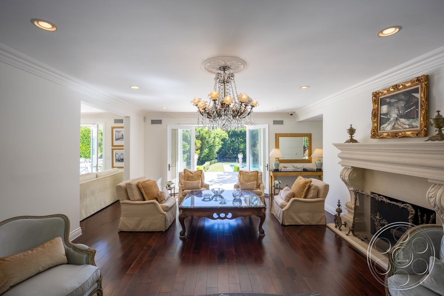 Americana 431 - landscaped garden view, decorative wall art, hardwood living room floors, interior living room, neutral painted walls, open floor plan design, stone fireplace surround, chandelier lighting fixture, exposed crown molding details, suburban residential setting, glass door leading to outdoor patio, luxury seating area with cream-colored upholstery, elegant coffee table with glass top, built-in mirrored wall unit, sunlit space with outdoor views, cozy family gathering area