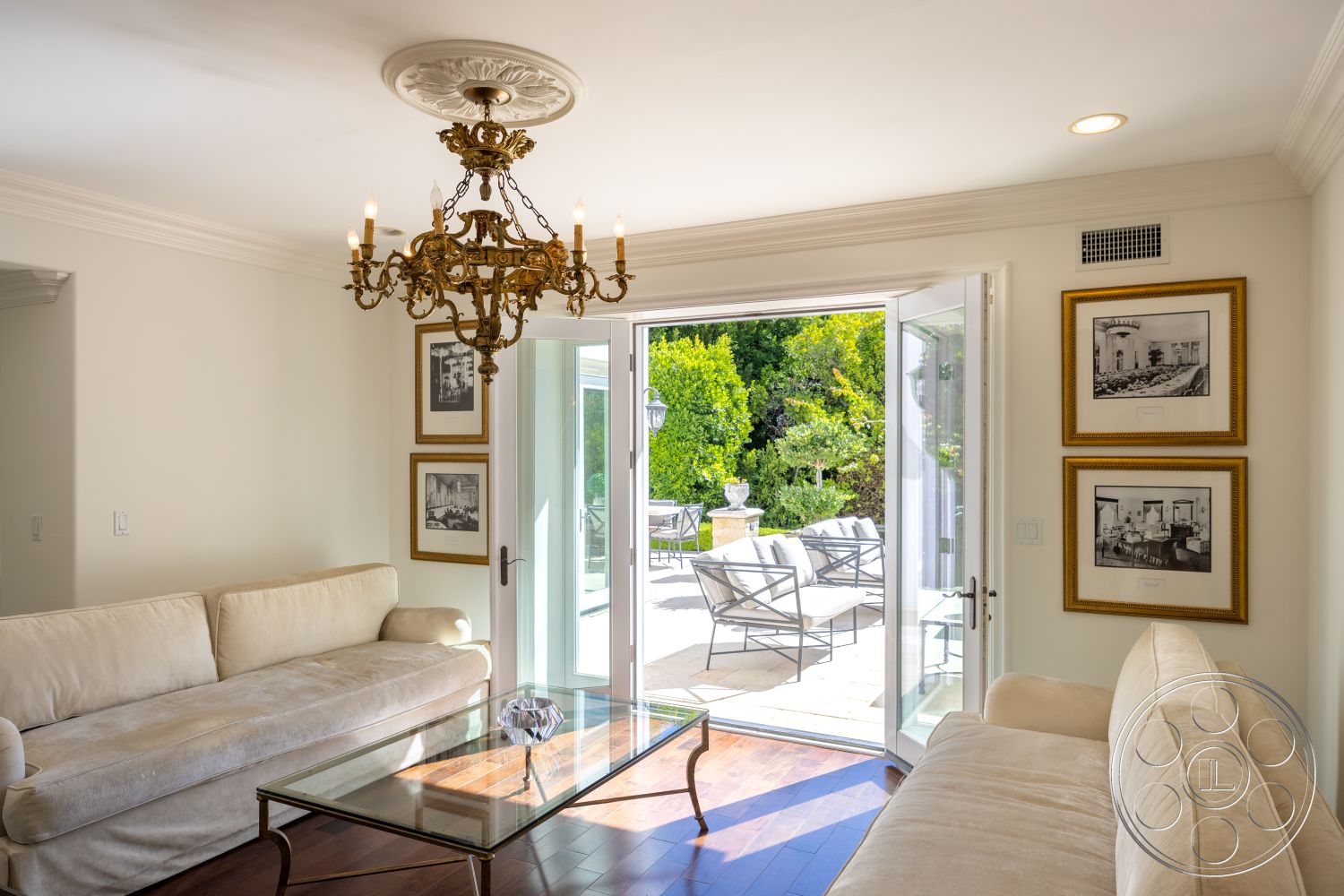 Americana 431 - minimalist decor, neutral color palette, natural light, spacious layout, glass coffee table, framed wall art, double French doors, decorative molding, ornate chandelier, classic aesthetic, outdoor patio view, interior living room, hardwood floor living room, coffered ceiling details, cream upholstered sofa, green landscaped setting, open indoor-outdoor flow