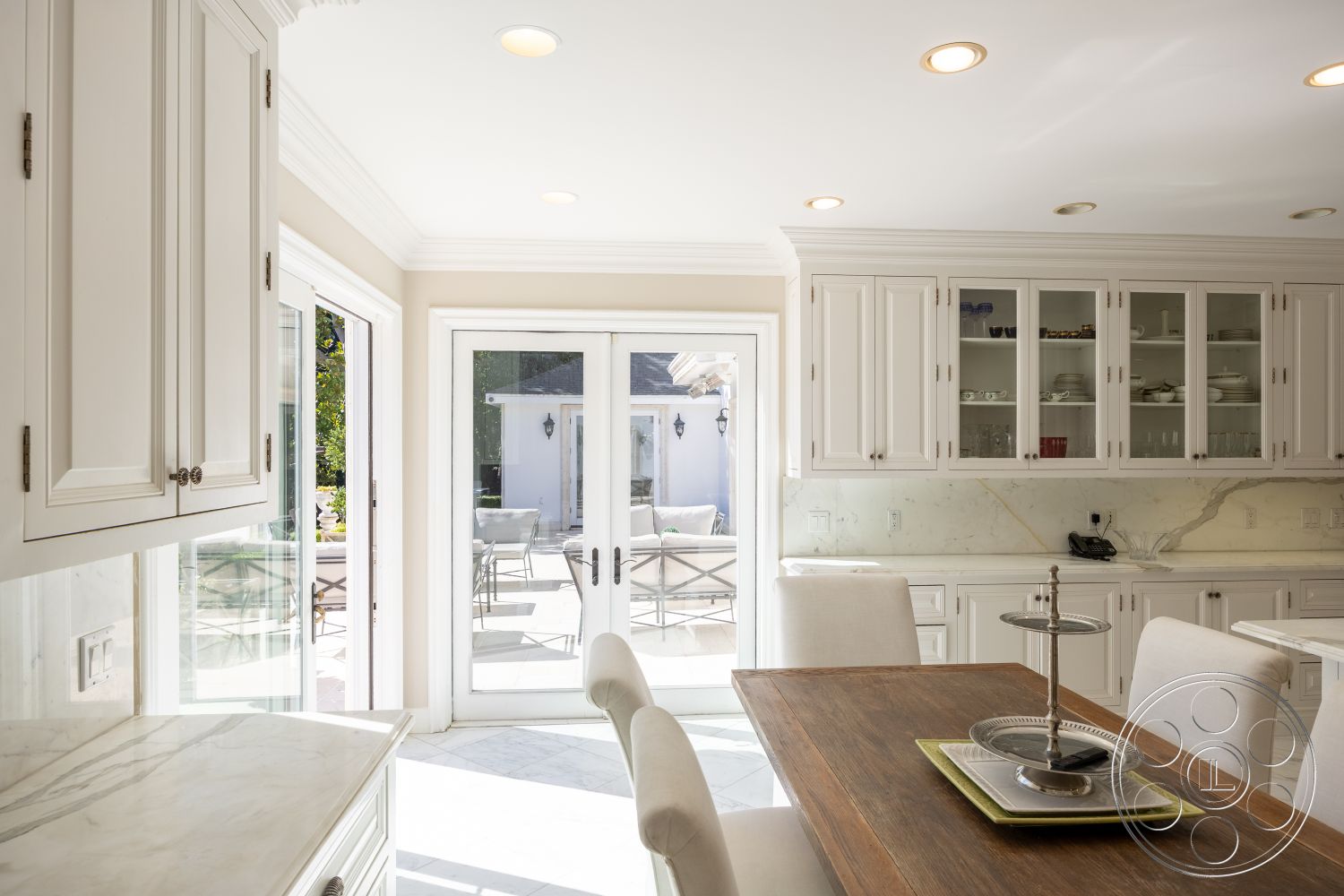 Americana 431 - bright and airy atmosphere, textured wall treatment, open-concept design, marble kitchen countertops, interior kitchen, natural light-filled space, modern kitchen style, outdoor patio access, crown molding details, brass cabinet hardware, glass French doors, hardwood dining table, ceramic tile kitchen flooring, white cabinetry with shaker doors