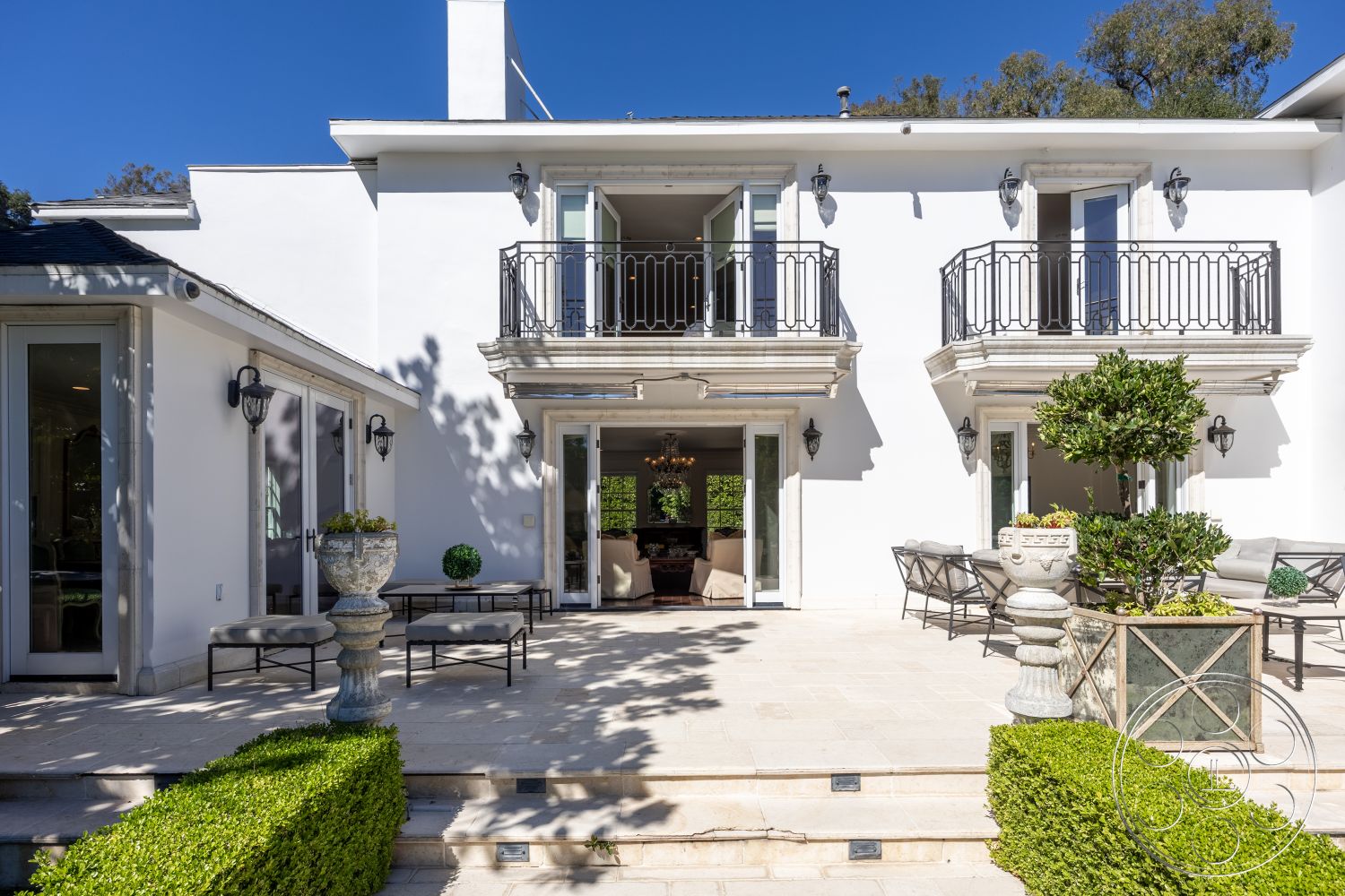 Americana 431 - exterior, modern outdoor furniture, formal garden setting, landscaped hedges, sloped roof design, white painted trim, symmetrical architectural layout, double glass doors, paved stone patio flooring, stucco house facade, stone stair steps, wrought iron balcony railings, ceramic outdoor tiles, traditional lantern wall sconces, elegant front porch design, ornate outdoor urns, greenery planters, clear blue sky background