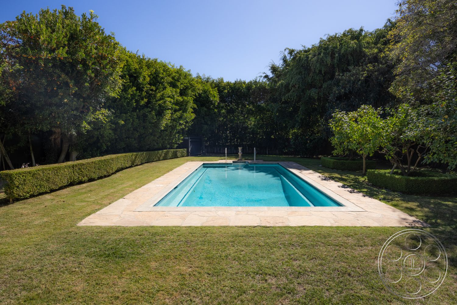 Americana 431 - rectangular swimming pool, sunlit pool area, outdoor relaxation area, lush garden setting, natural grass lawn, exterior stone pool deck, private backyard oasis, surrounding trees and foliage, hedged landscape border