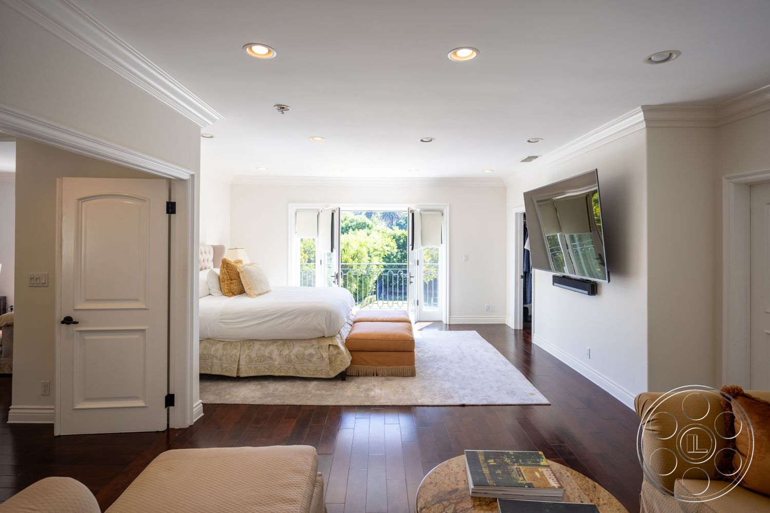 Americana 431 - neutral color palette, floor-to-ceiling windows, plush area rug, balcony view, cozy sitting area, hardwood bedroom floors, white painted walls, crown molding details, modern wall-mounted television, queen-sized bed with decorative pillows, elegant decorative ottoman, spacious master suite