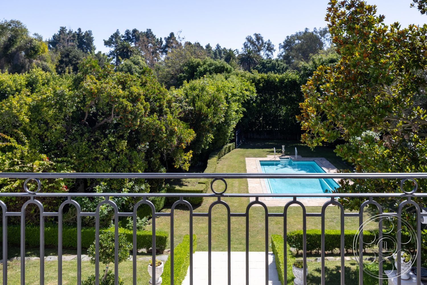 Americana 431 - exterior, rectangular swimming pool, mature trees, grassy yard, stone pool deck, sunny outdoor setting, hedge border, outdoor leisure space, flower planters, lush landscaped garden, metal balcony railing