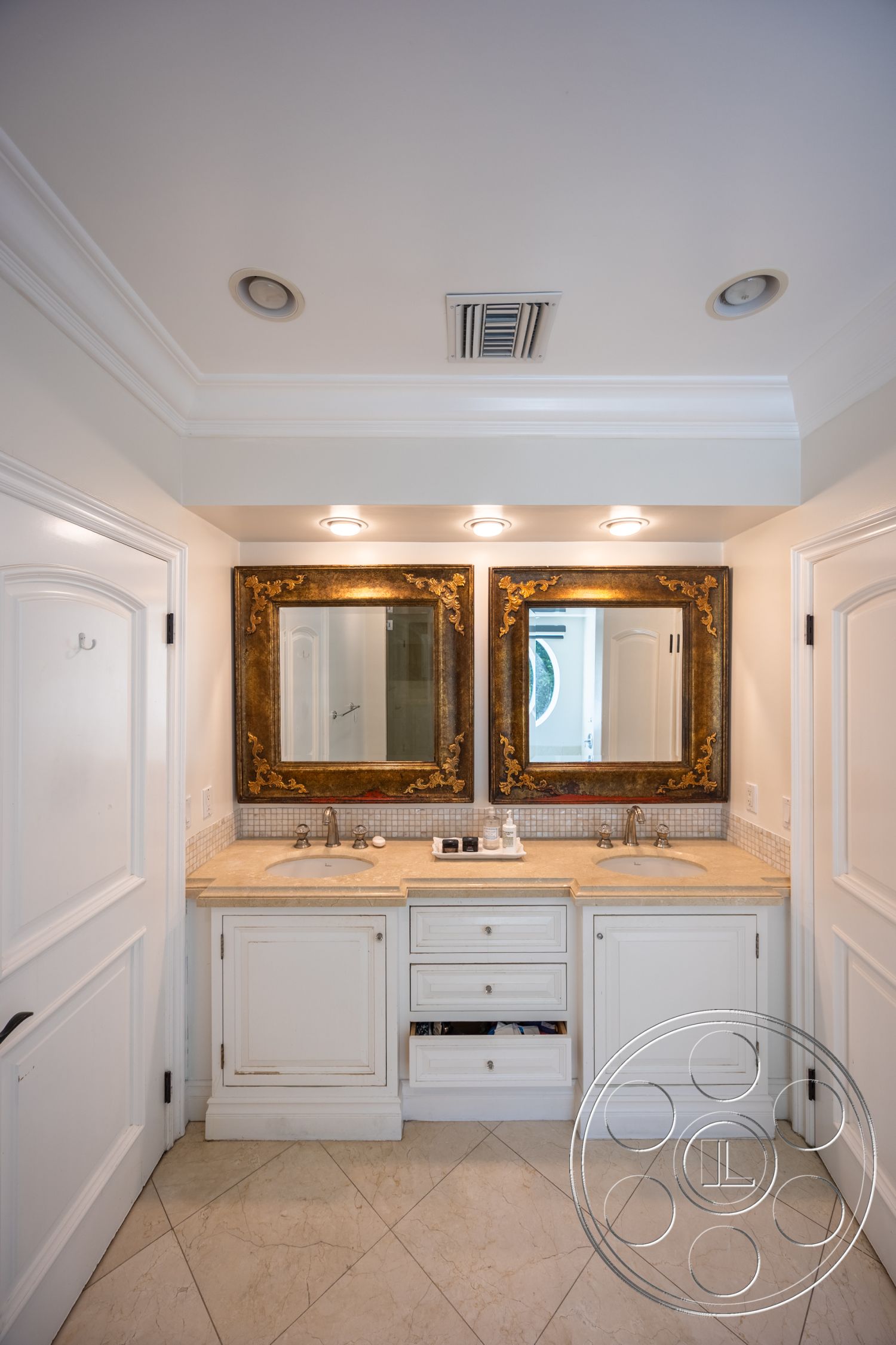 Americana 431 - neutral color palette, recessed ceiling lighting, interior bathroom, white painted walls, crown molding details, marble tile flooring, quartz countertop vanity, double vanity sinks, framed wall mirrors, modern sink faucets, textured backsplash tile, built-in drawer storage, traditional cabinet design