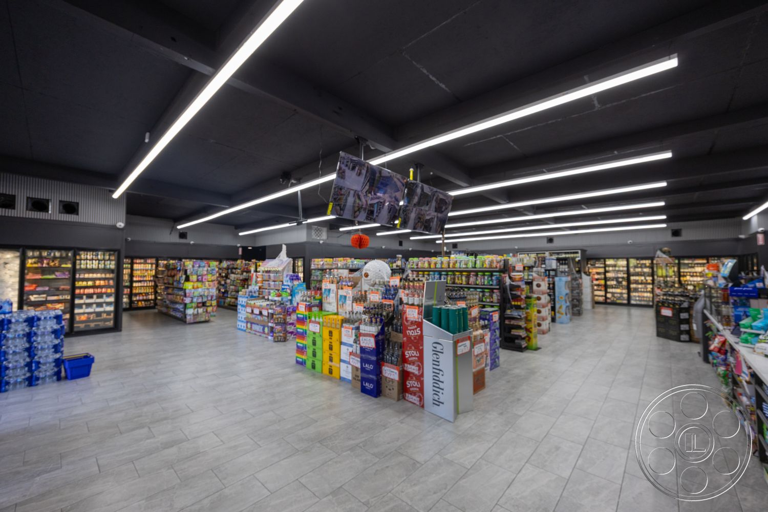 Shop 127 - minimalist design elements, metal shelving units, polished tile flooring, open floor plan layout, exposed black ceiling, LED strip lighting, interior grocery store, glass refrigeration units, modern retail display, light gray tiled walls, product signage overhead, rectangular store layout, curved checkout counter, aisle organization for products, brightly lit shopping environment