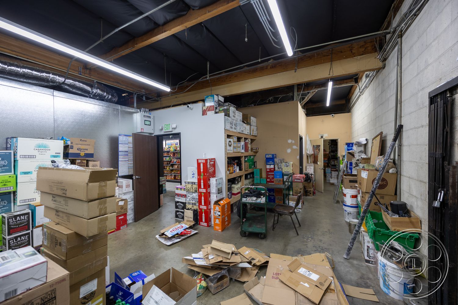 Shop 127 - open floor plan, concrete block walls, metal ductwork, wood beam ceiling, exposed concrete flooring, fluorescent ceiling lights, interior warehouse space, utility room, industrial shelving units, functional utility area, cardboard box storage, exit door, stacked storage boxes