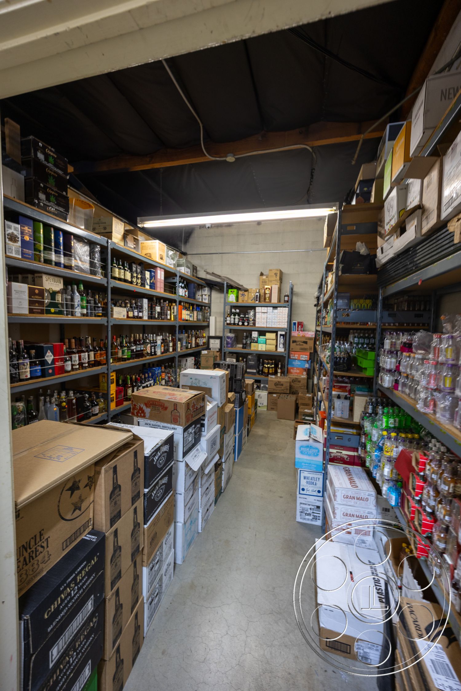 Shop 127 - minimalist design, shelving units, concrete flooring, ambient lighting, high ceiling, organized clutter, storage boxes, fluorescent overhead lighting, narrow aisle layout, functional storage space, warehouse interior, industrial structure, flat ceiling with exposed beams, packed inventory, branded packaging, commercial storage area, organized shelving, grey cinder block walls, universal design, retail stockroom, high-traffic area