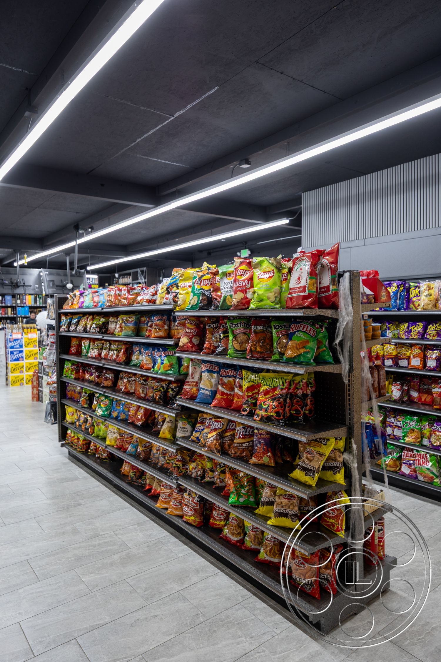 Shop 127 - neutral color palette, open layout, fluorescent lighting, industrial style, metal shelving units, laminate flooring, exposed concrete ceiling, high ceiling design, LED strip lighting, rectangle display layout, grocery store setting, well-organized snack aisle, package display, brightly colored packaging, clean and modern aesthetic