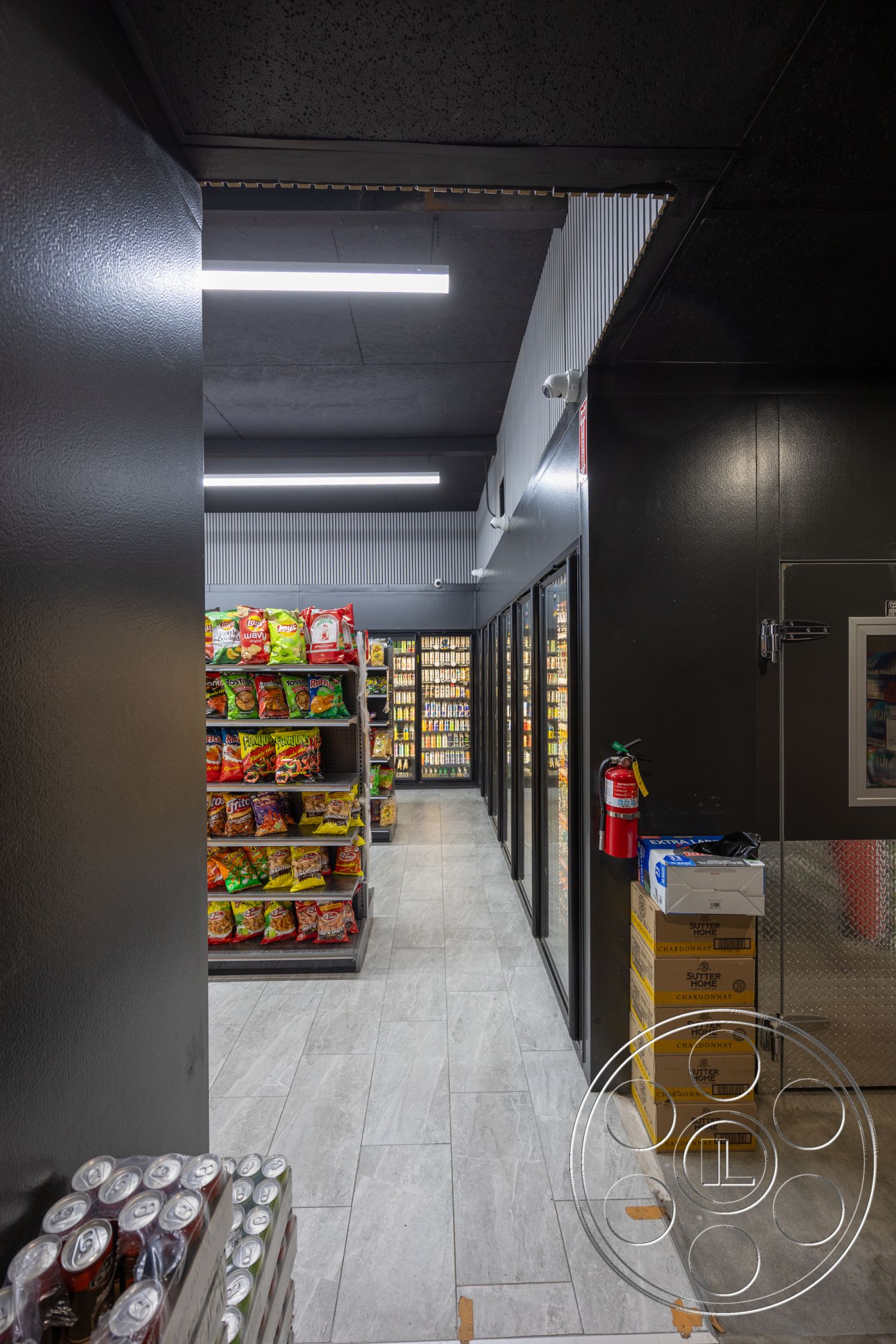 Shop 127 - metal shelving units, black painted ceiling, interior grocery store space, strip lighting fixtures, tile flooring with gray pattern, glass front refrigerator doors, dark glossy wall finish, exposed steel frame, fire extinguisher mounted, stacked beverage cans, corner shelving for snacks, aluminum composite panel wall, minimalist aisle layout, modern retail design, functional storage spaces