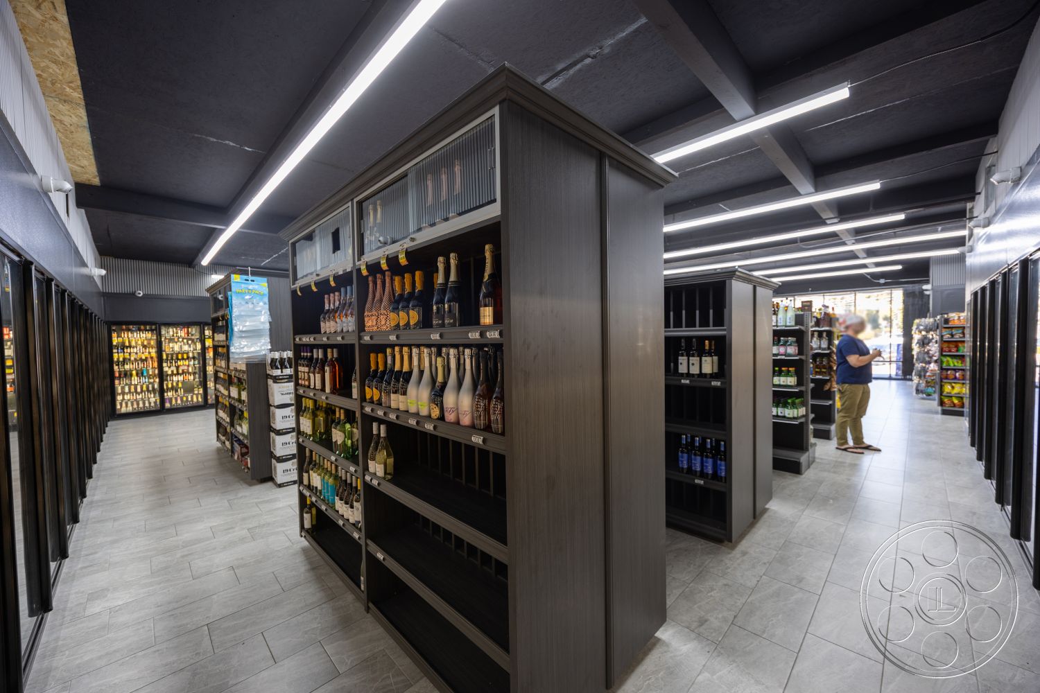 Shop 127 - neutral color palette, exposed beam ceiling, minimalist design elements, concrete block walls, shiplap accent wall, glass storefront entrance, interior retail space, linear floor plan, modern industrial aesthetic, flush-mounted ceiling lights, polished porcelain tile flooring, suspended LED lighting fixtures, dark wood shelving units, open retail layout, frosted glass display cases, commercial beverage cooler sections, corridor between aisles, product display shelving, smart merchandising layout, customer interaction area