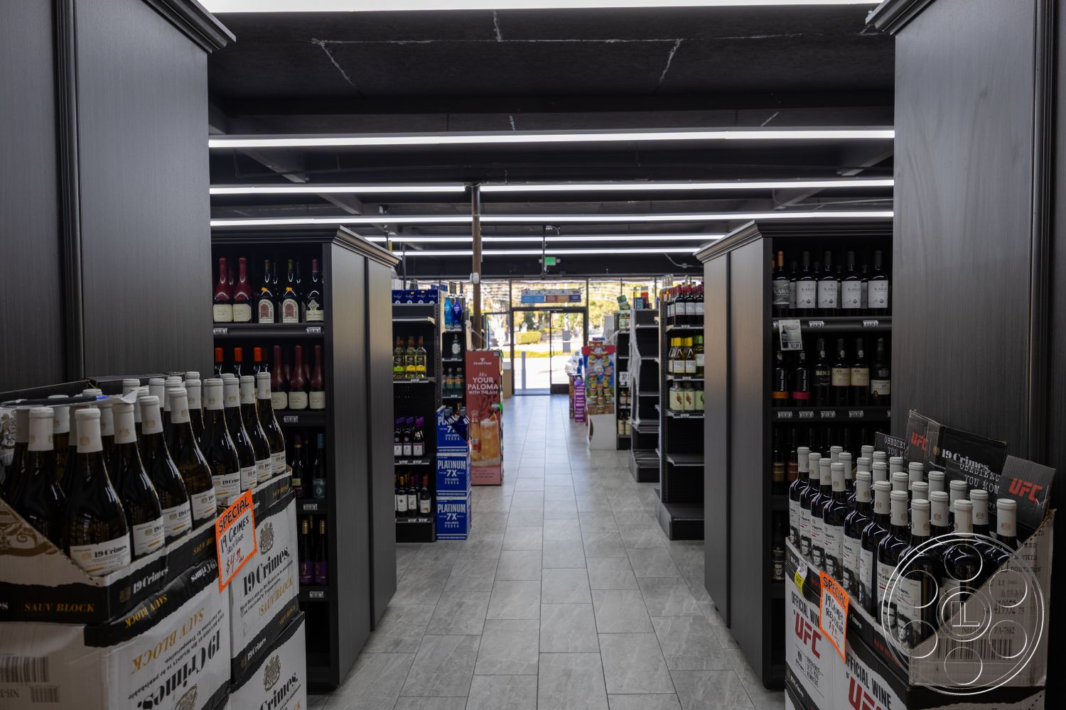 Shop 127 - minimalist aesthetic, custom cabinetry, laminate flooring, open floor plan layout, large storefront windows, urban retail environment, ample natural light, LED strip lighting, modern retail design, interior liquor store, high-gloss black ceiling, dark wood display shelves, glass-front refrigerator units, tiled sales floor, product aisle, wine display racks, intense lighting contrast, easy-access product arrangement, bottle signage displays