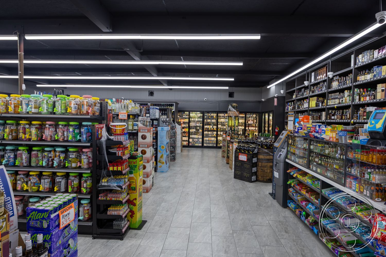 Shop 127 - open floor plan, interior space, metal shelving units, industrial style interior, LED ceiling lighting, commercial retail design, sleek tile flooring, rectangular floor layout, glass refrigerator doors, black acoustic ceiling tiles, wood accent displays, modern cash register area, various beverage containers, organized product displays, colorful packaging arrangements, efficiency in layout, customer-friendly navigation