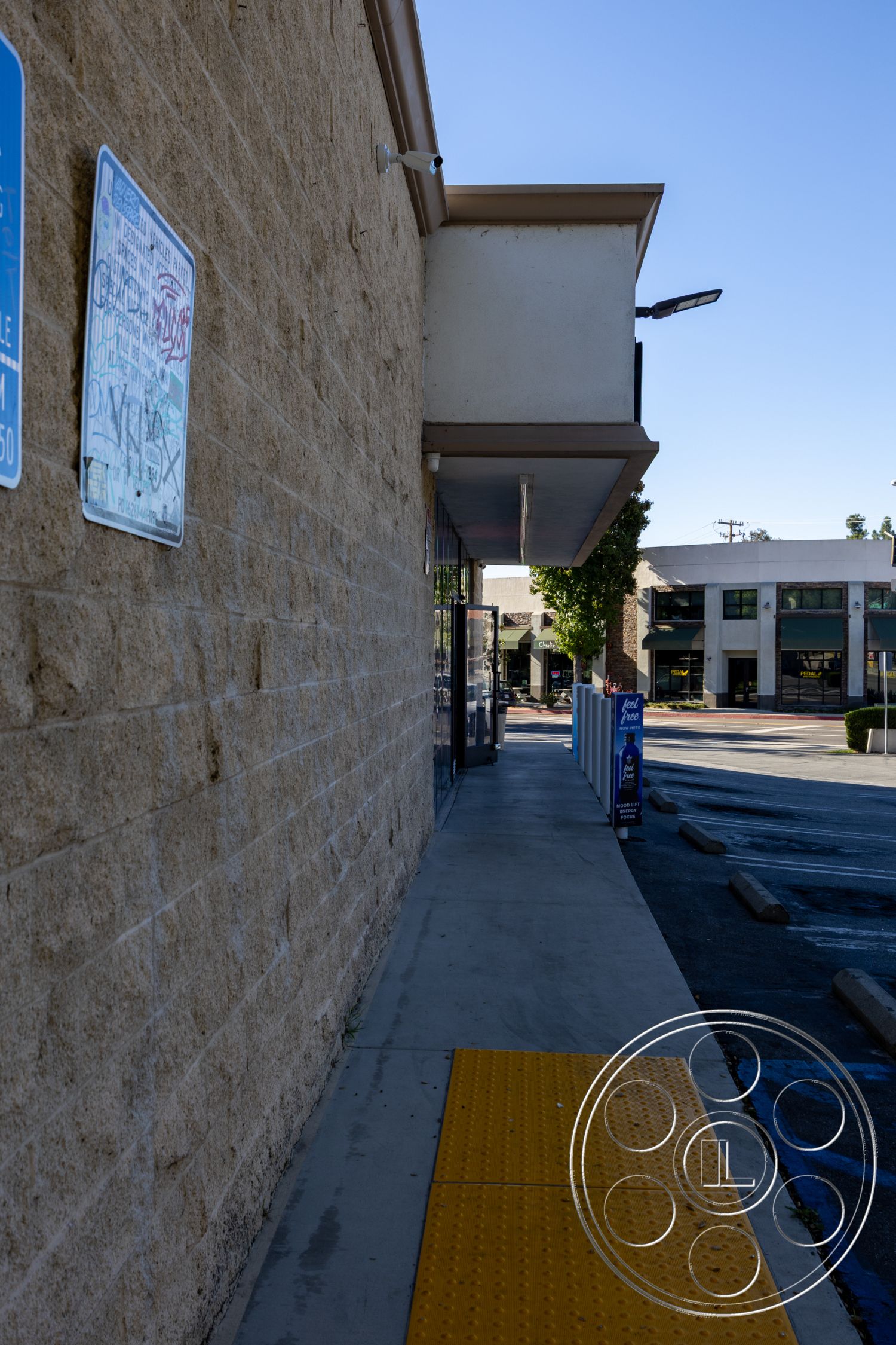 Shop 127 - flat roof overhang, glass storefront windows, open sky view, commercial building setting, exterior concrete block walls, exterior stucco finish, concrete sidewalk with tactile paving, metal exterior signage, urban storefront entrance, yellow safety pedestrian path, surrounding urban parking lot, adjacent two-story buildings, city infrastructure backdrop