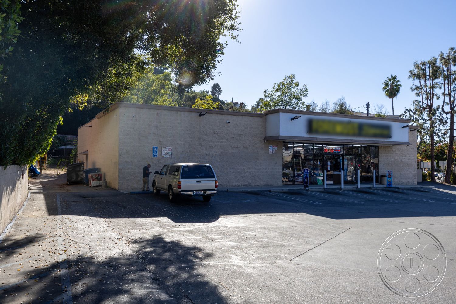 Shop 127 - ambient natural light, flat roof design, large glass storefront windows, concrete parking lot surface, exterior concrete block walls, landscaped tree surrounds, street-side accessibility features, functional commercial space, urban commercial environment, desert climate adaptation, city backdrop setting