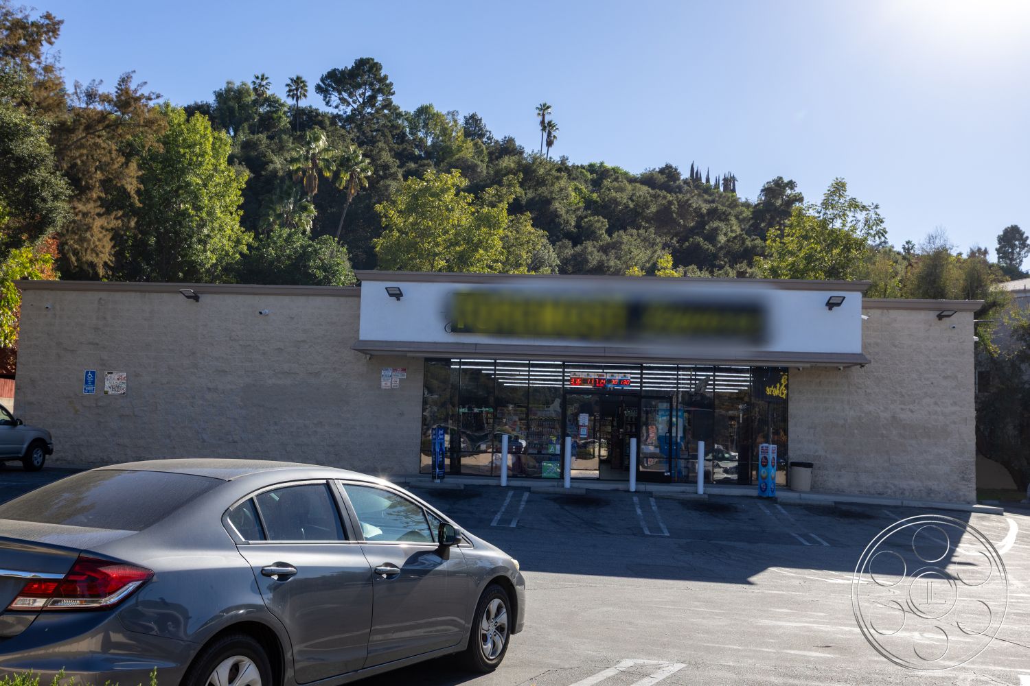 Shop 127 - landscaped greenery, asphalt driveway, concrete parking lot, accessible parking space, stucco exterior walls, flat roof structure, urban commercial setting, exterior building facade, large glass storefront windows, surrounding hillside vegetation, modern retail design, paved pedestrian access, vibrant outdoor signage, single-story commercial building