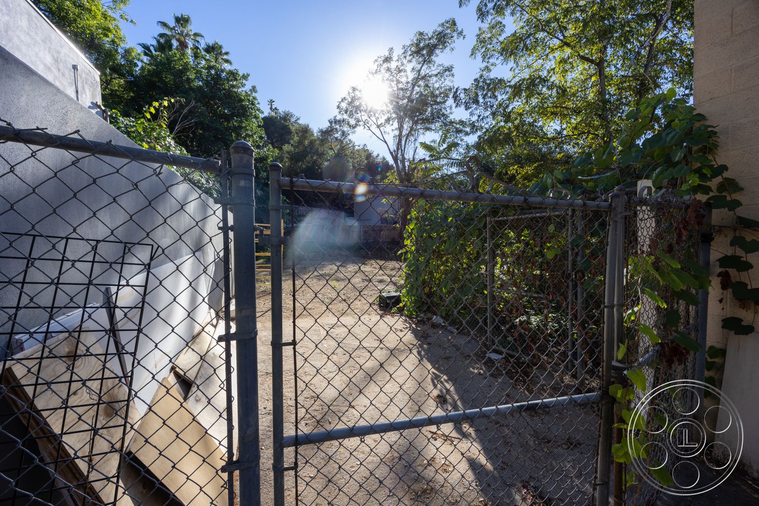 Shop 127 - natural light, greenery landscaping, informal outdoor area, access gate, sunlit outdoor space, urban backyard setting, surrounding trees and foliage, chain link fence exterior, concrete ground surface, exposed aggregate flooring, weathered building materials, partial wall exposure, low-maintenance outdoor environment, asphalt paving, rusted metal features