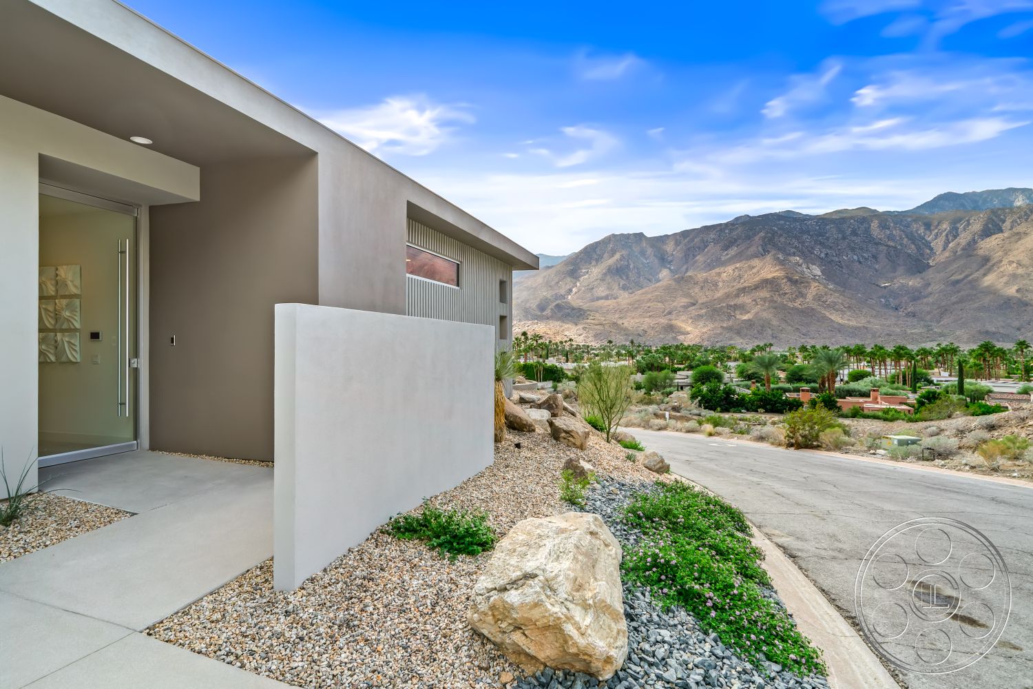 Palm Springs 109 - contemporary architectural style, mountain view setting, modern minimalist design, exterior concrete walkway, exterior smooth stucco walls, desert mountain backdrop, floor-to-ceiling glass entry door, desert landscaping with drought-resistant plants, gravel and rock garden, smooth concrete curb, angular wall treatment, light-colored concrete finish, palm trees in surrounding area, low-maintenance xeriscape, exterior angular details, smooth stone feature borders