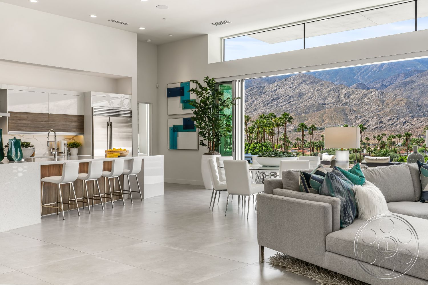 Palm Springs 109 - modern light fixtures, seamless indoor-outdoor living, open floor plan living area, grey porcelain tile flooring, desert mountain backdrop, light-filled dining area, interior kitchen with quartz countertops, stainless steel appliances in modern kitchen, floor-to-ceiling windows with mountain views, contemporary bar seating, white-painted walls with minimalist decor, decorative potted plants for interior greenery, plush grey sectional sofa in living room, textured throw pillows on sofa, light-filled space with natural light, executive style dining table, sliding glass doors opening to patio, urban desert home environment, stylish open concept design