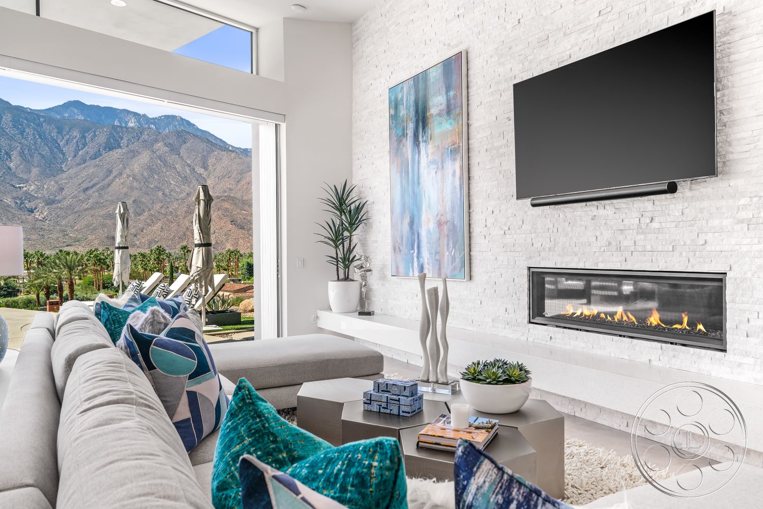 Palm Springs 109 - high ceilings, neutral color palette, spacious layout, stone accent wall, wall-mounted television, large glass windows, open concept design, seating area, indoor/outdoor flow, luxury finishes, textured throw pillows, mountain view, large sliding glass doors, light gray area rug, decorative plant accents, contemporary sectional sofa, natural light infusion, modern living room, white brick feature wall, minimalist fireplace design, silver coffee table, artwork with blue tones, exposed beam detail, outdoor pool area visibility