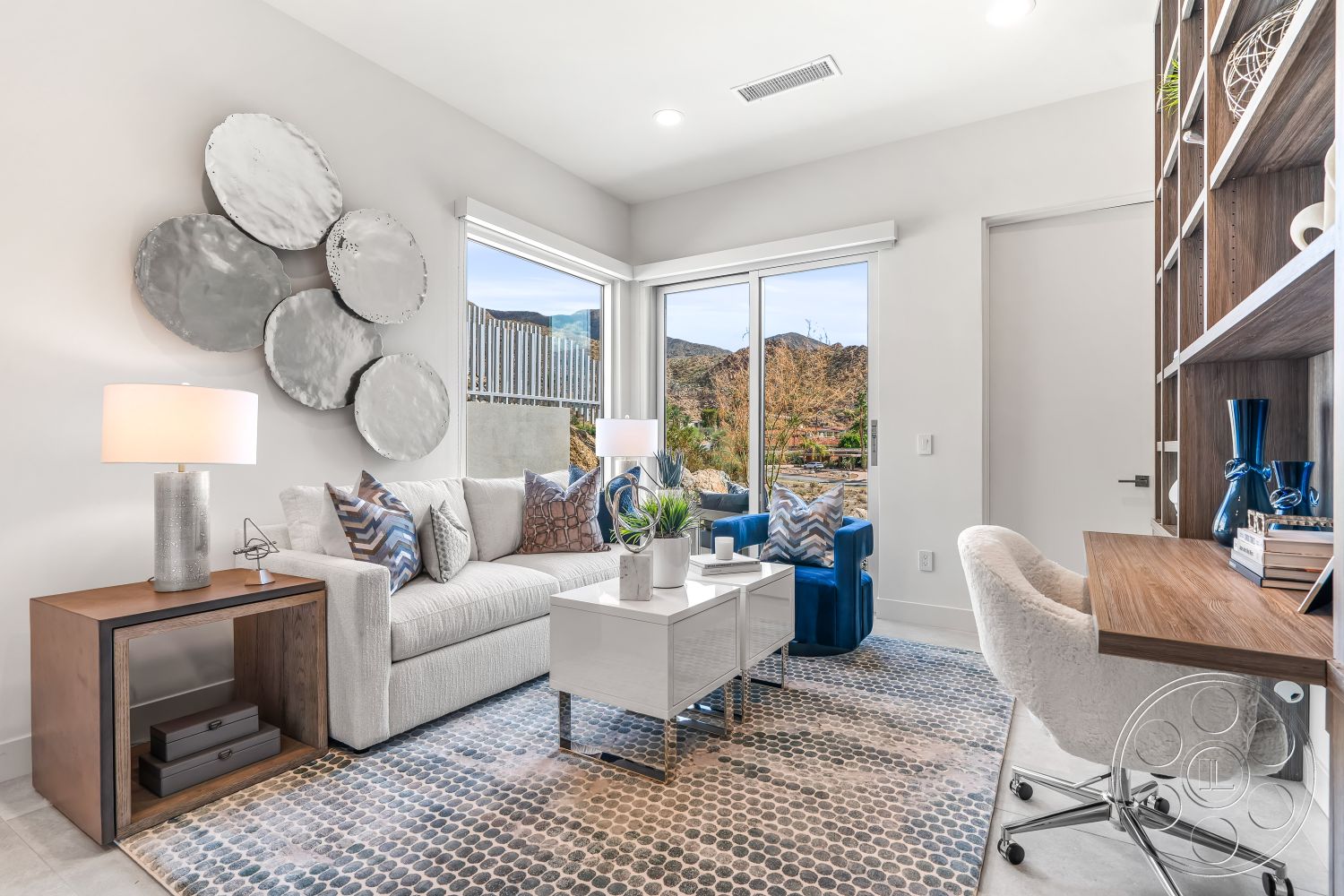 Palm Springs 109 - round coffee table, polished concrete flooring, floor-to-ceiling windows, minimalist desk, textured throw pillows, soft ambient lighting, blue accent chairs, wooden side table, interior living room, modern sofa, built-in shelving unit, light gray painted walls, exposed aggregate area rug, metallic wall art, natural mountain view