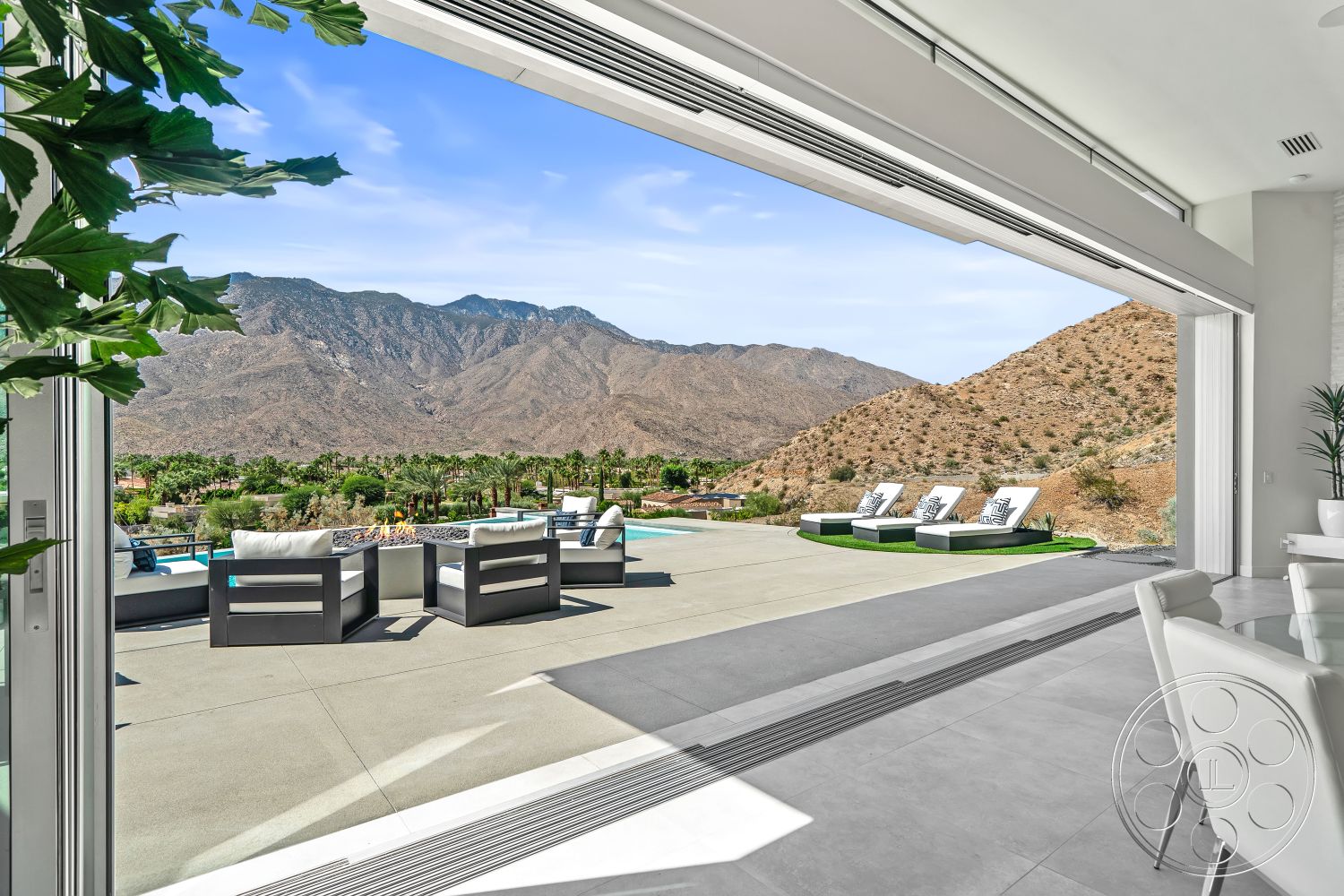 Palm Springs 109 - landscaped garden, ceramic tile flooring, rectangular swimming pool, modern outdoor seating, natural stone retaining wall, mountain view setting, concrete patio flooring, open floor plan design, sliding glass doors interior, vaulted ceiling interior, glass window wall, desert landscape environment, sleek modern architecture, exterior lounge area with fire pit, white walls interior, poolside chaise lounges, green turf lawn, poured concrete terrace