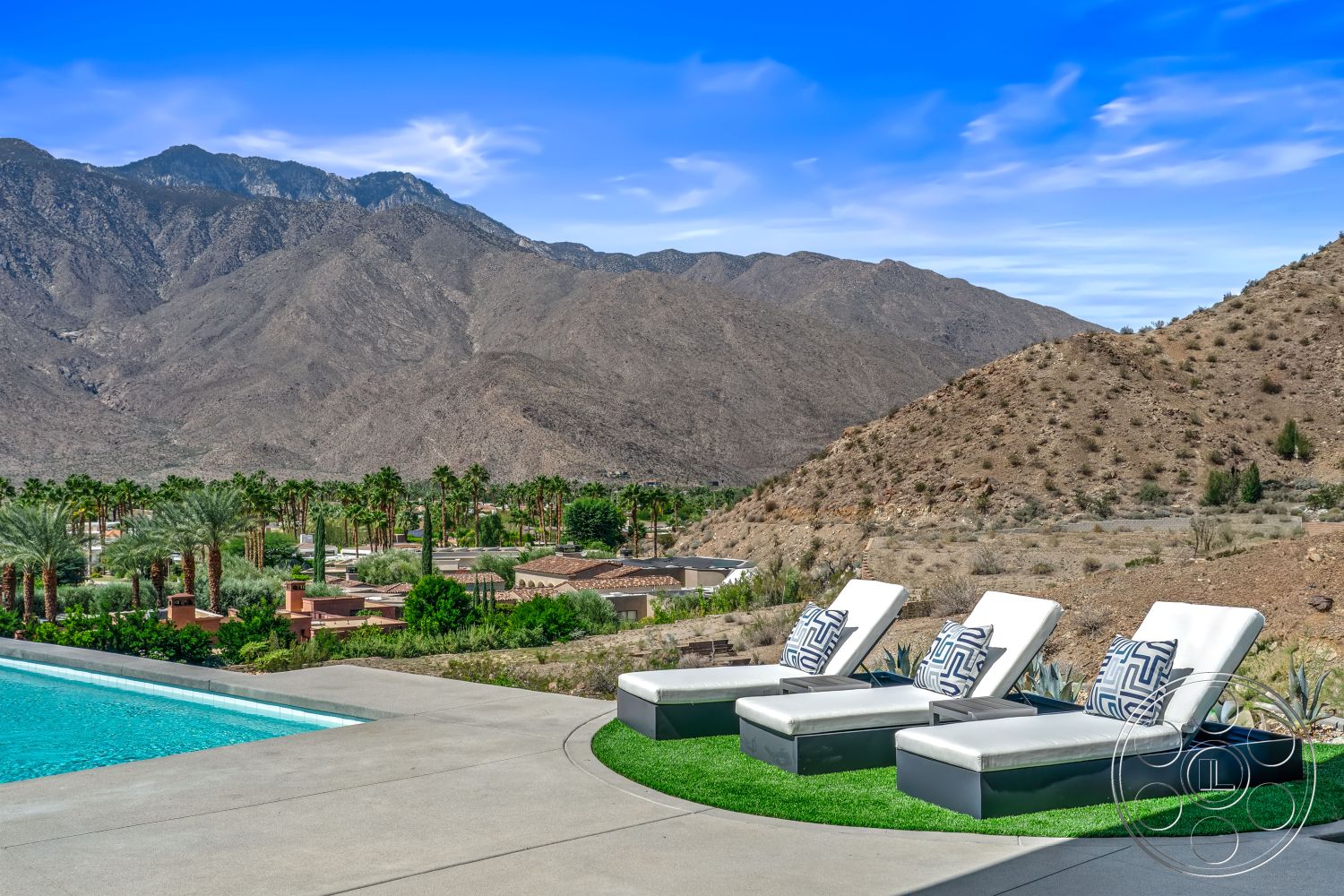 Palm Springs 109 - sloped terrain, rectangular swimming pool, landscaped backyard, mountain backdrop, clear blue sky, concrete pool deck, desert setting, sun-drenched patio, sleek modern design, urban residential neighborhood, palm trees landscaping, luxury outdoor living space, exterior pool area, modern outdoor lounge chairs, artificial grass patio