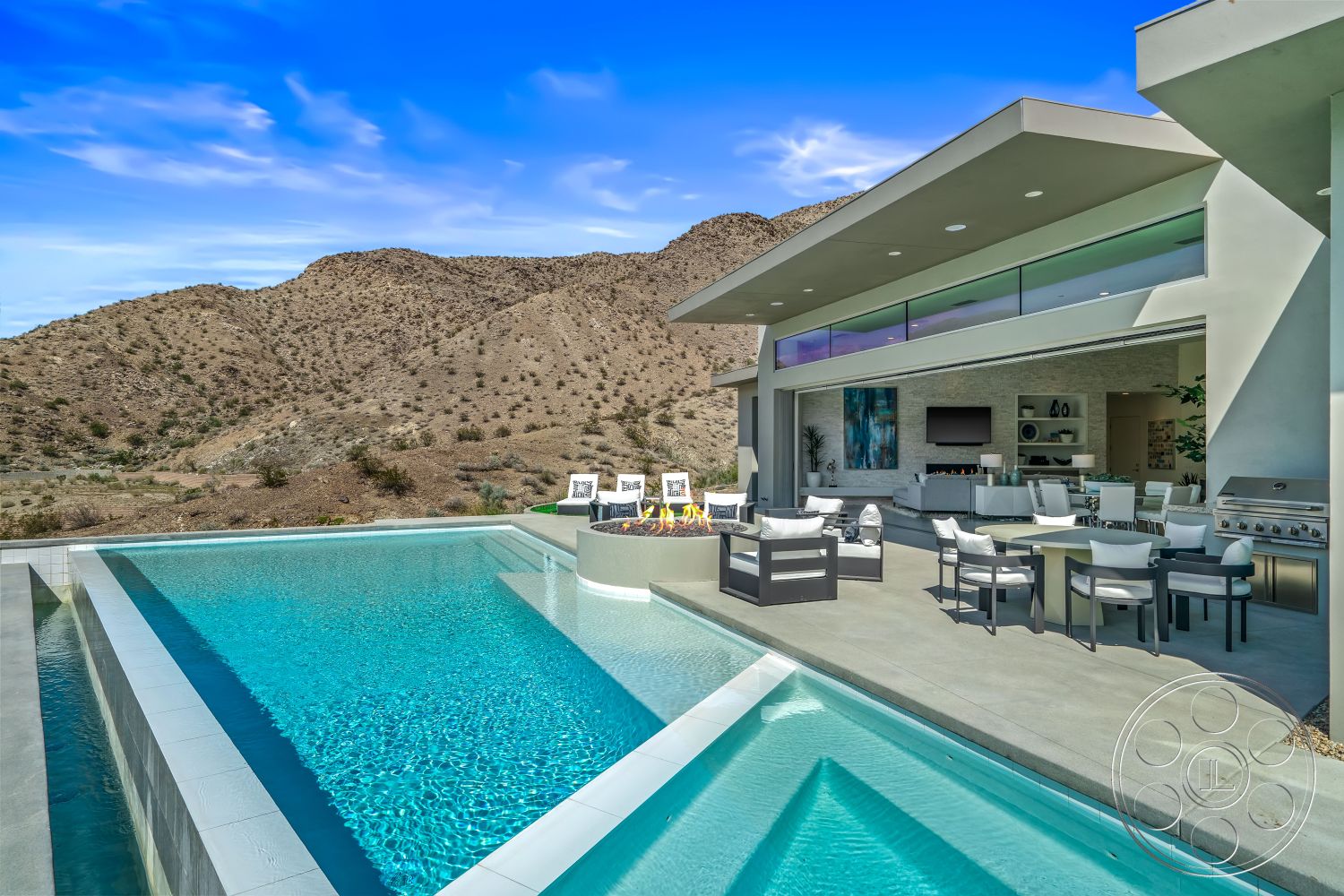 Palm Springs 109 - exterior, stone accent wall, glass sliding doors, modern outdoor furniture, landscaped yard, floor-to-ceiling windows, mountain backdrop, infinity pool, open-concept layout, hardscape design, rectangular pool, minimalist architecture, contemporary architectural style, concrete fire pit, concrete pool border, concrete patio floor, stainless steel outdoor grill, sunny outdoor living area, desert home setting, breezy mountain view