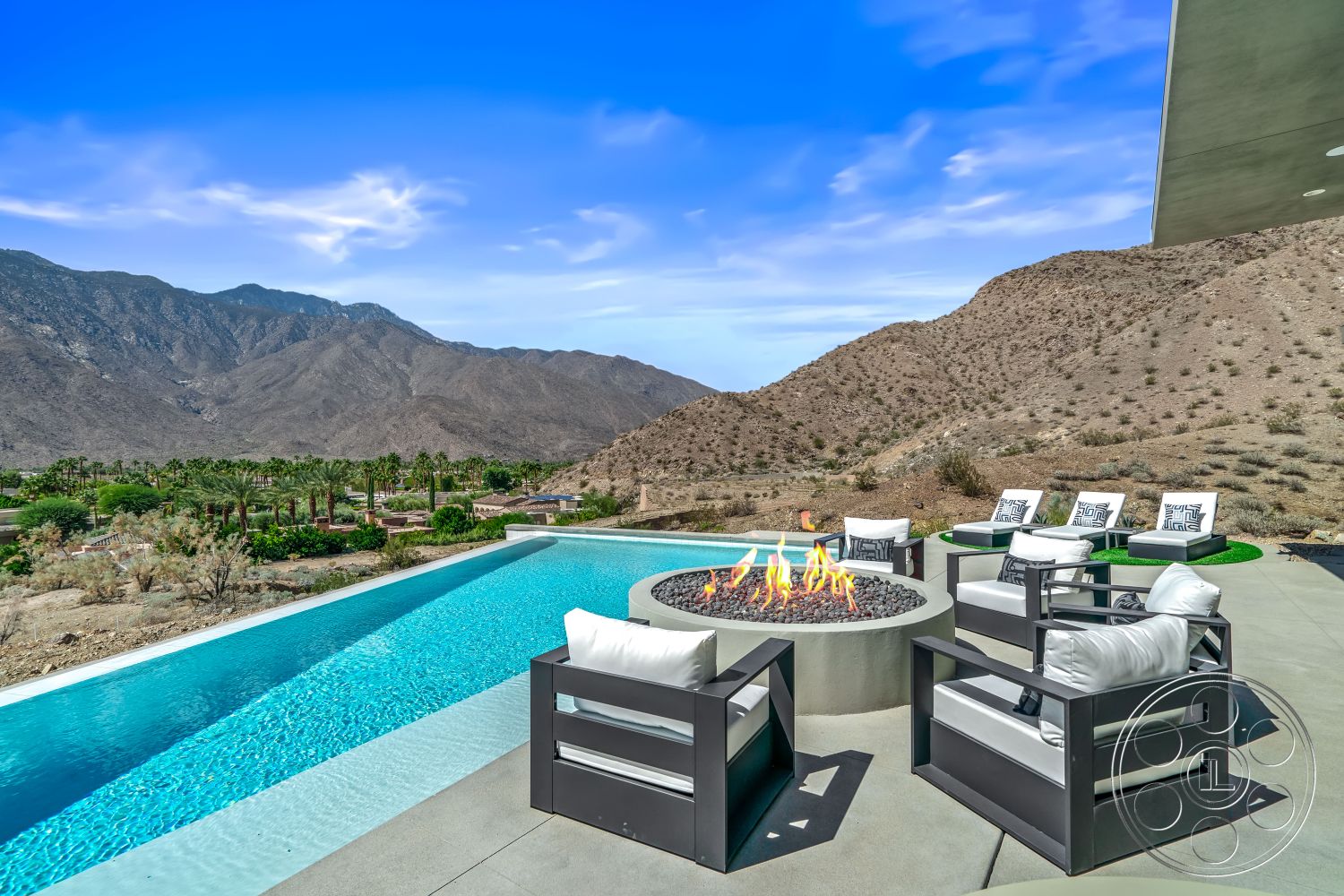 Palm Springs 109 - clear blue sky, infinity edge pool, mountain view backdrop, minimalist outdoor lounge area, rectangular pool design, desert landscape setting, exterior concrete swimming pool, gray concrete patio flooring, contemporary fire pit with stone surround, modern aluminum seating with cushions, zero-edge pool perimeter, slate stone terrace, landscaped poolside garden, green lawn turf for outdoor seating, daylight illumination, valley and mountain scenery