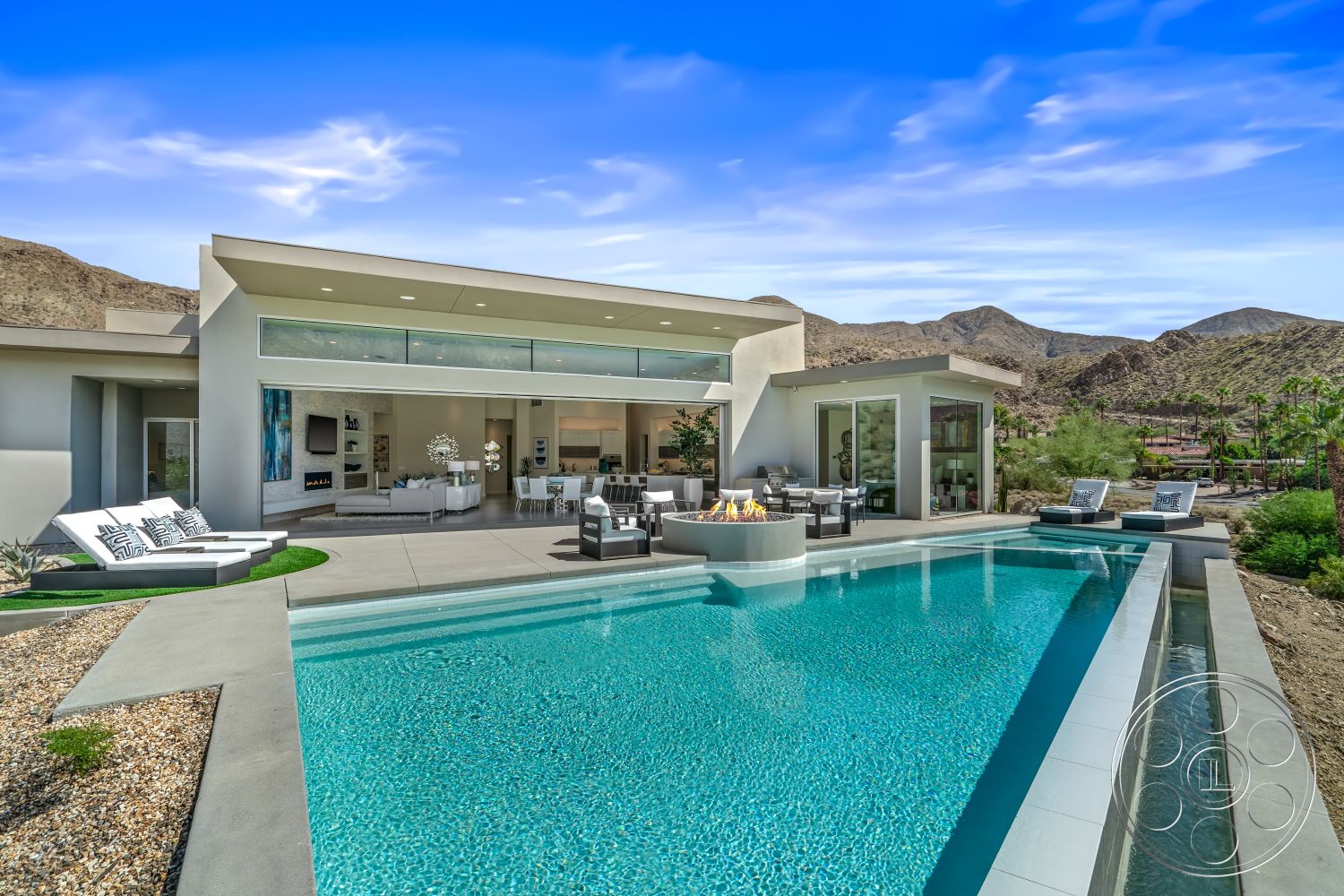 Palm Springs 109 - exterior, modern architecture, exposed beam ceiling, glass sliding doors, rectangular swimming pool, large floor-to-ceiling windows, circular fire pit, concrete patio floor, minimalist outdoor furniture, sunny outdoor seating area, high ceilings with recessed lighting, mountain view backdrop, open plan living space, landscaped desert setting, polished concrete pool deck, desert landscaping with gravel, neutral color palette for exterior, stylish outdoor lounge chairs, integrated outdoor fire feature, varied terrain with low shrubs