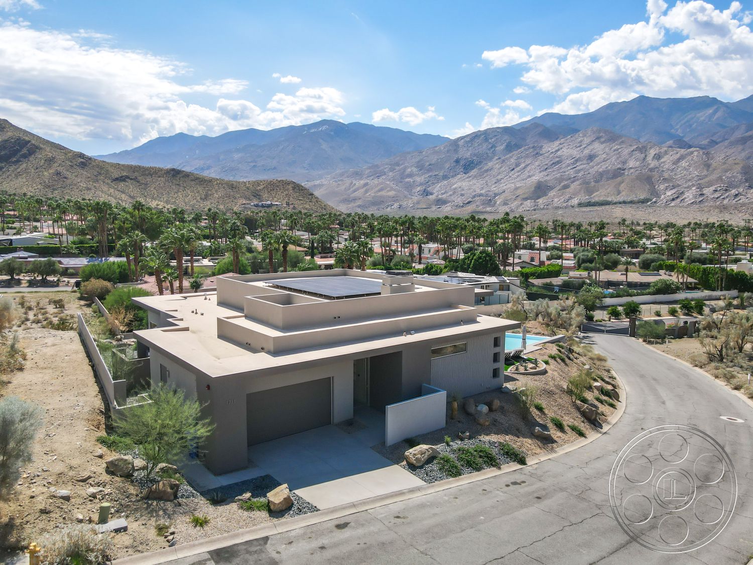 Palm Springs 109 - minimalist design elements, modern architectural style, concrete driveway, open parking area, flat roof design, stucco exterior walls, mountain view backdrop, palm tree surroundings, exterior lighting fixtures, desert landscape setting, solar panel array, designed for energy efficiency, hardscape rock features, cul-de-sac location, low-maintenance xeriscaped gardens